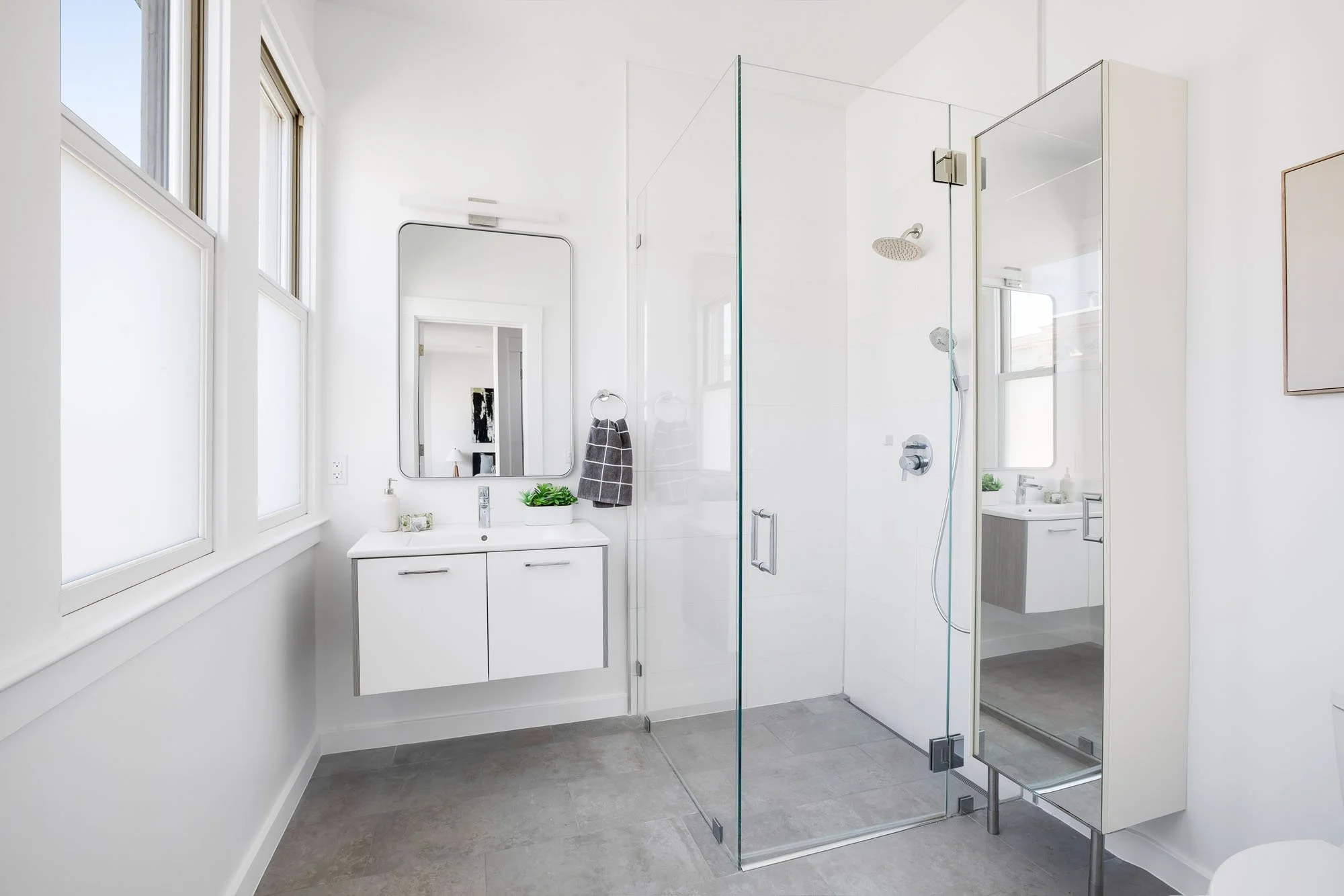 Luxury ensuite bathroom featuring a frameless glass walk-in shower, grey tile flooring, and a white modern vanity.
