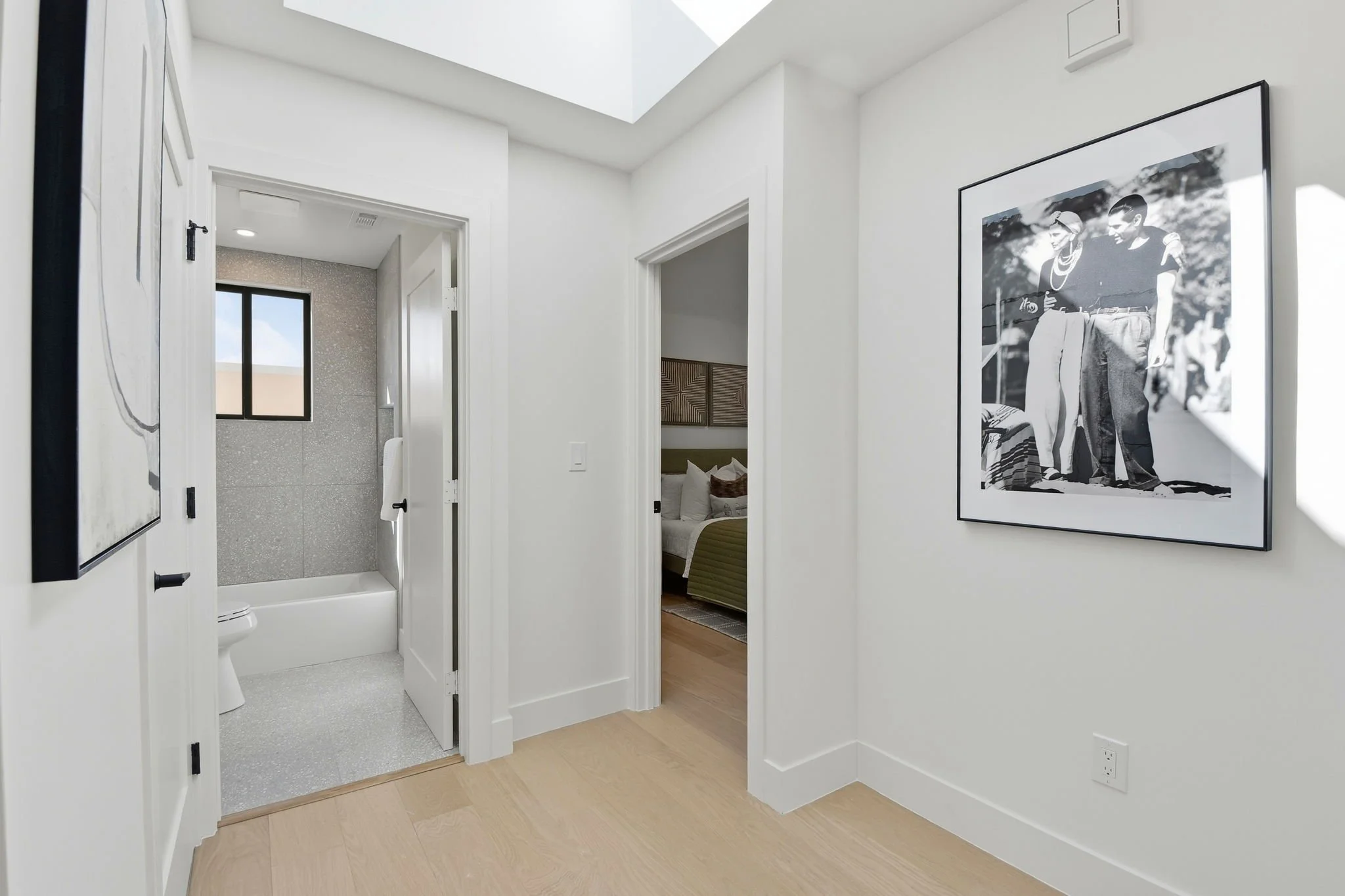 Bright modern hallway in a Midtown Terrace home featuring light oak flooring, designer artwork, and a view into a renovated guest bathroom.