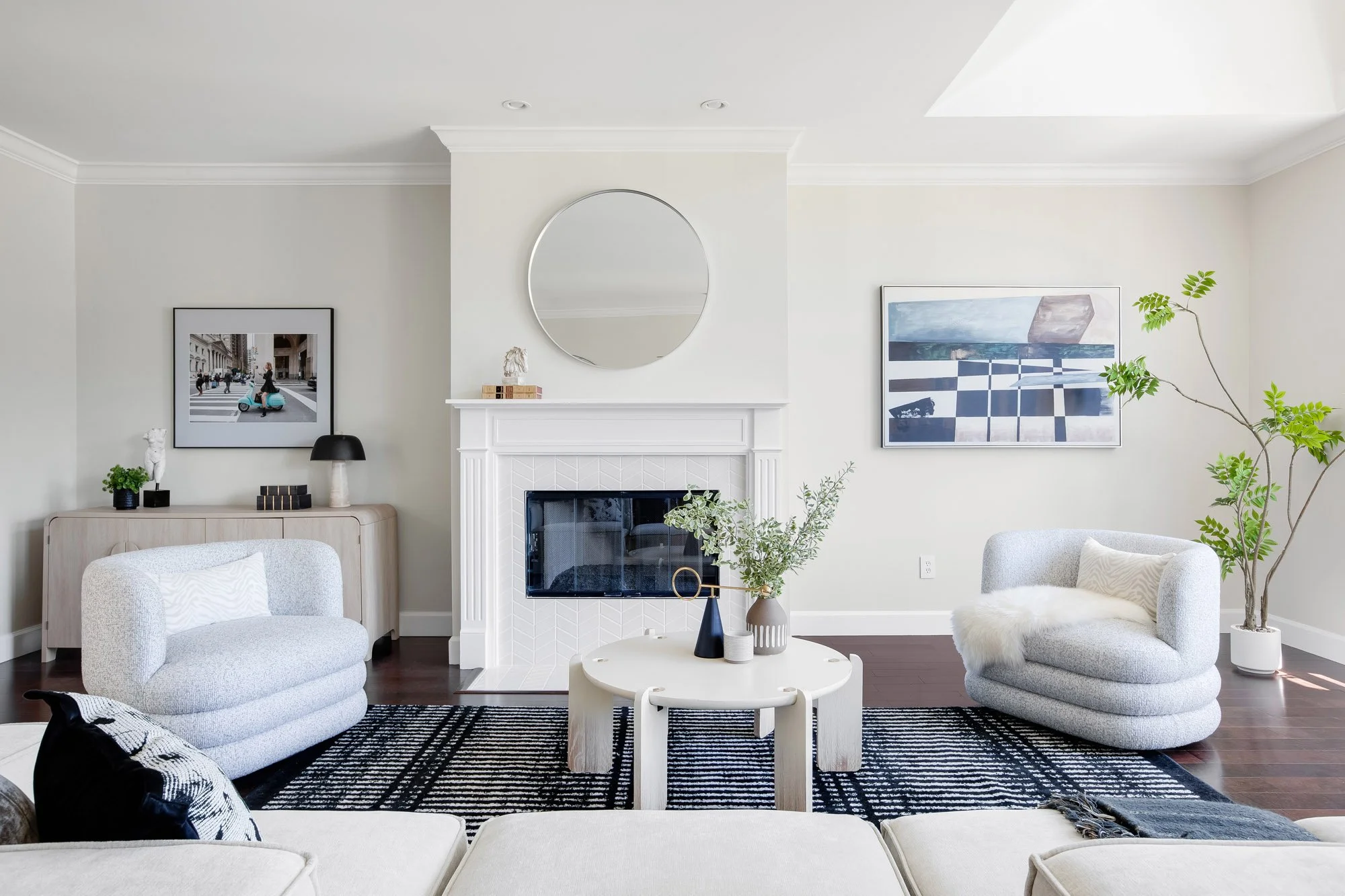 Living room sitting area at 2172 Fell Street San Francisco centered on a white herringbone fireplace with round mirror, paired boucle armchairs, skylight, and curated contemporary wall art