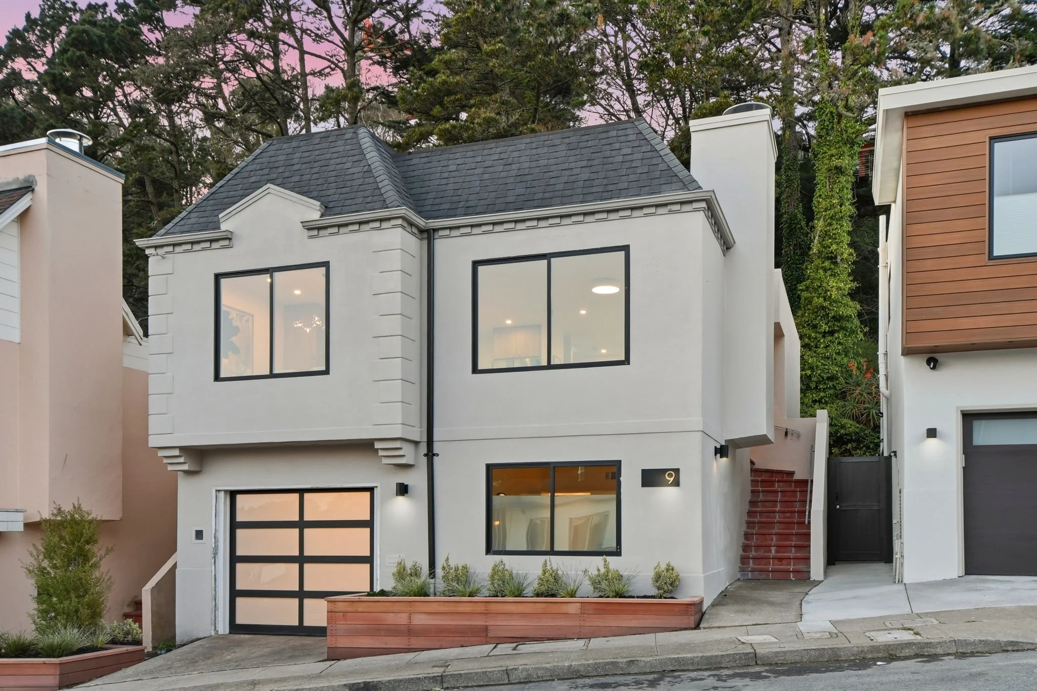 Sophisticated home facade in Midtown Terrace at dusk, showing bright, open interiors through large black-trimmed picture windows.