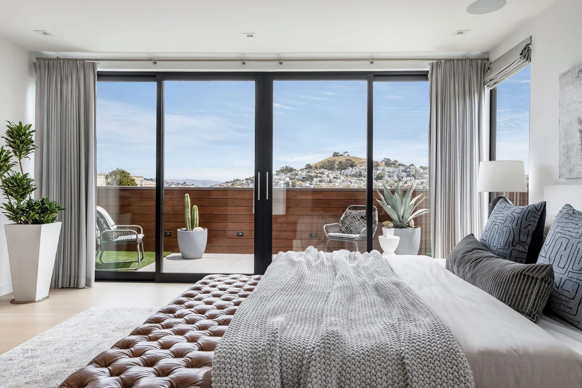 Primary bedroom suite at 1647 Sanchez featuring a tufted leather bench and expansive sliding glass doors that lead to a private sun deck with San Francisco city views.