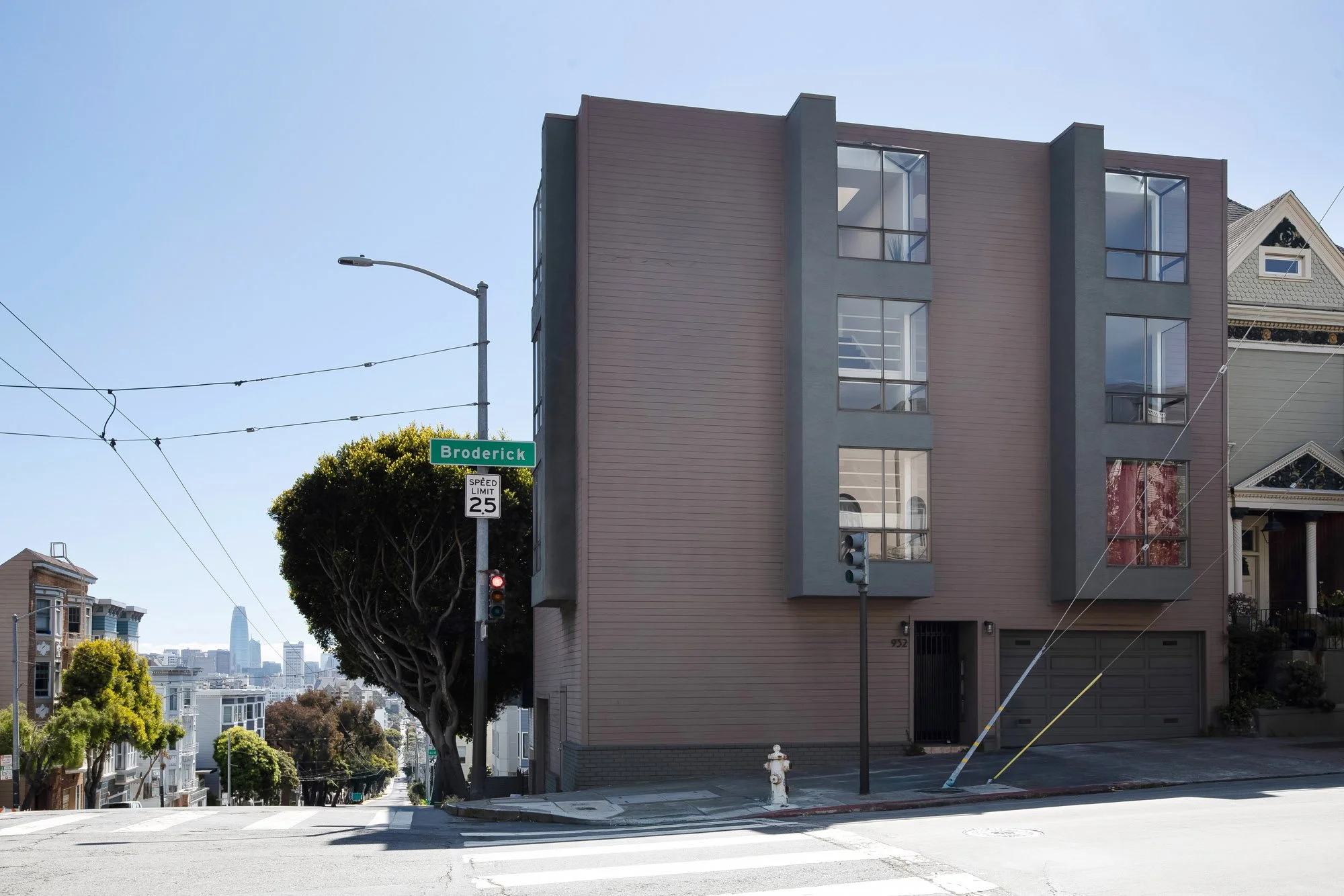 Street-level view of 932 Broderick Street condo building with downtown San Francisco skyline visible down the hill, in the Alamo Square/NoPa area.