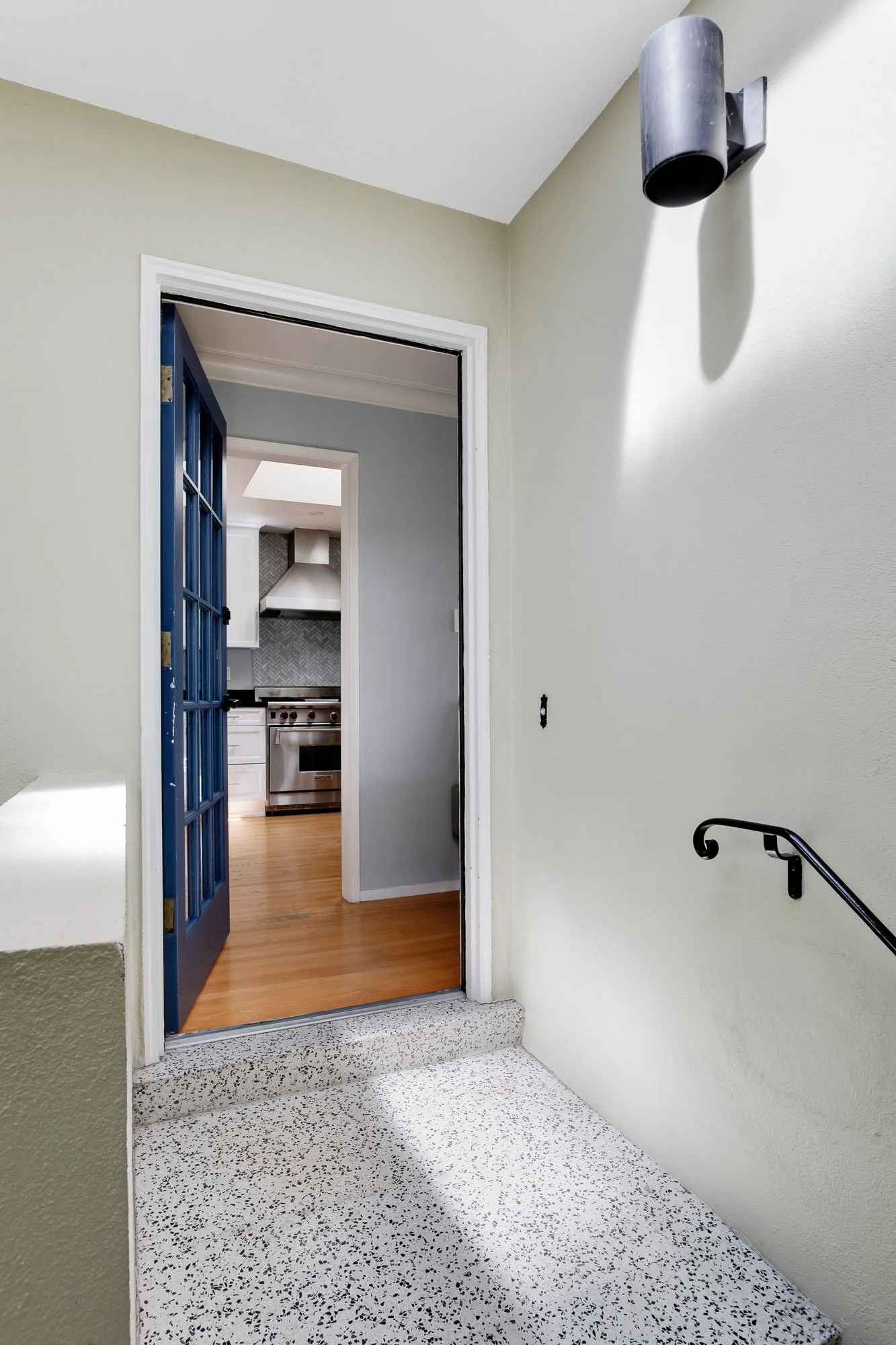 Interior view of the private entry landing with terrazzo flooring and a navy blue French door that opens into the bright, modern kitchen.