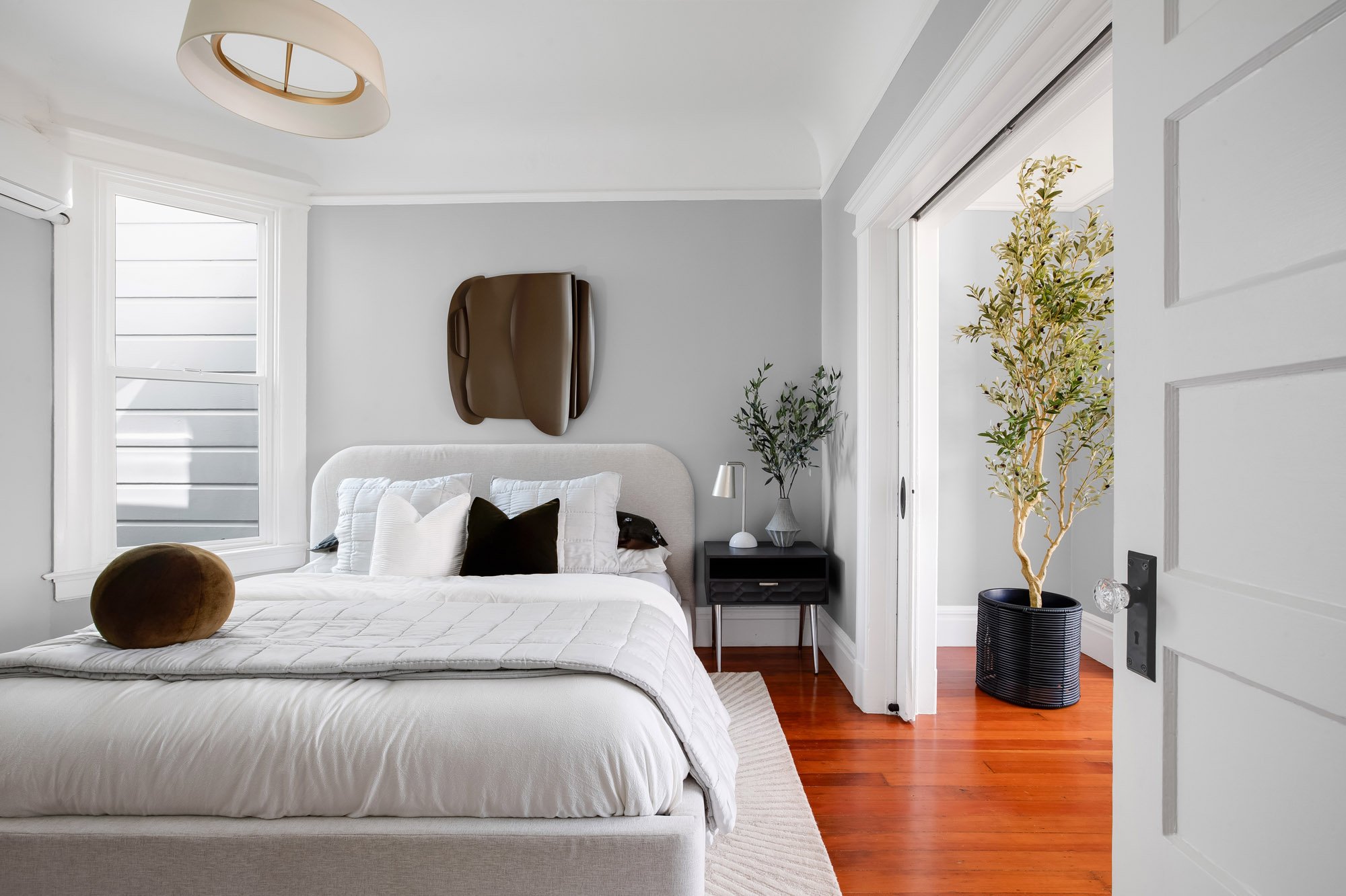 Bedroom with wall-mounted mini-split unit, olive tree, and glass-paned door open to the Living Room