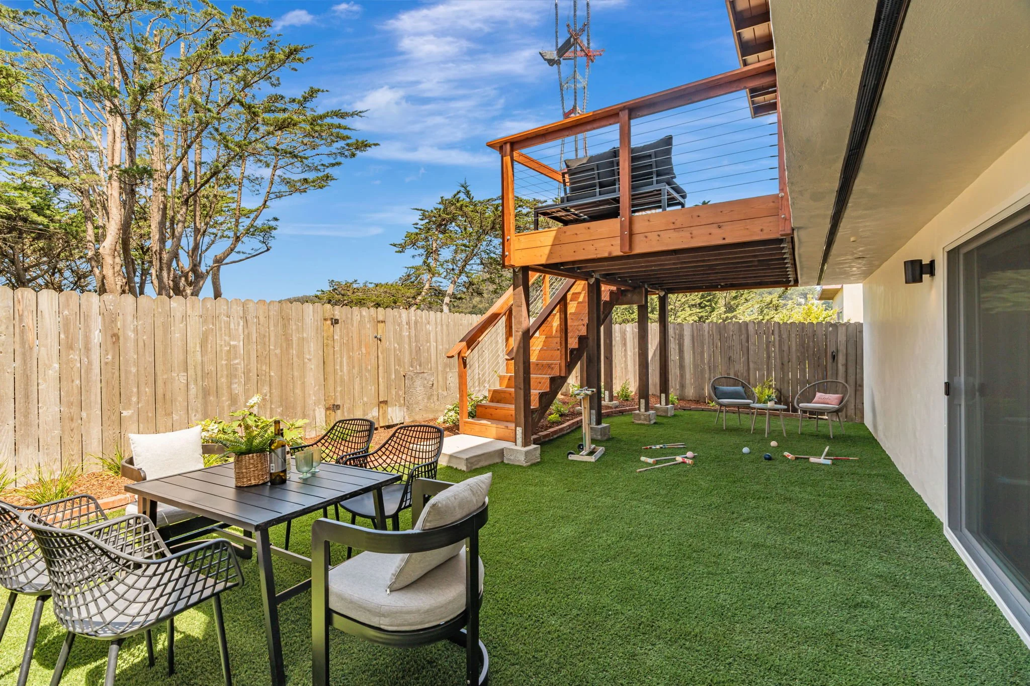 Private San Francisco backyard design featuring high-quality artificial turf, a black outdoor dining set, and a wooden staircase leading to a cantilevered upper-level deck.