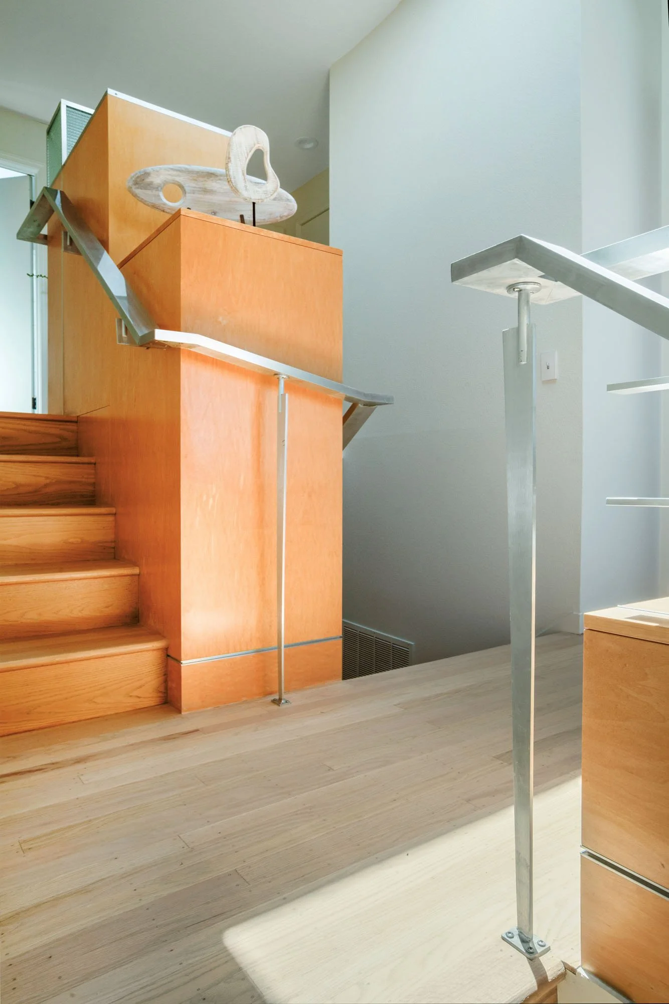Architectural detail of a contemporary home staircase featuring light oak wood treads and sleek custom metal handrails under natural skylight.