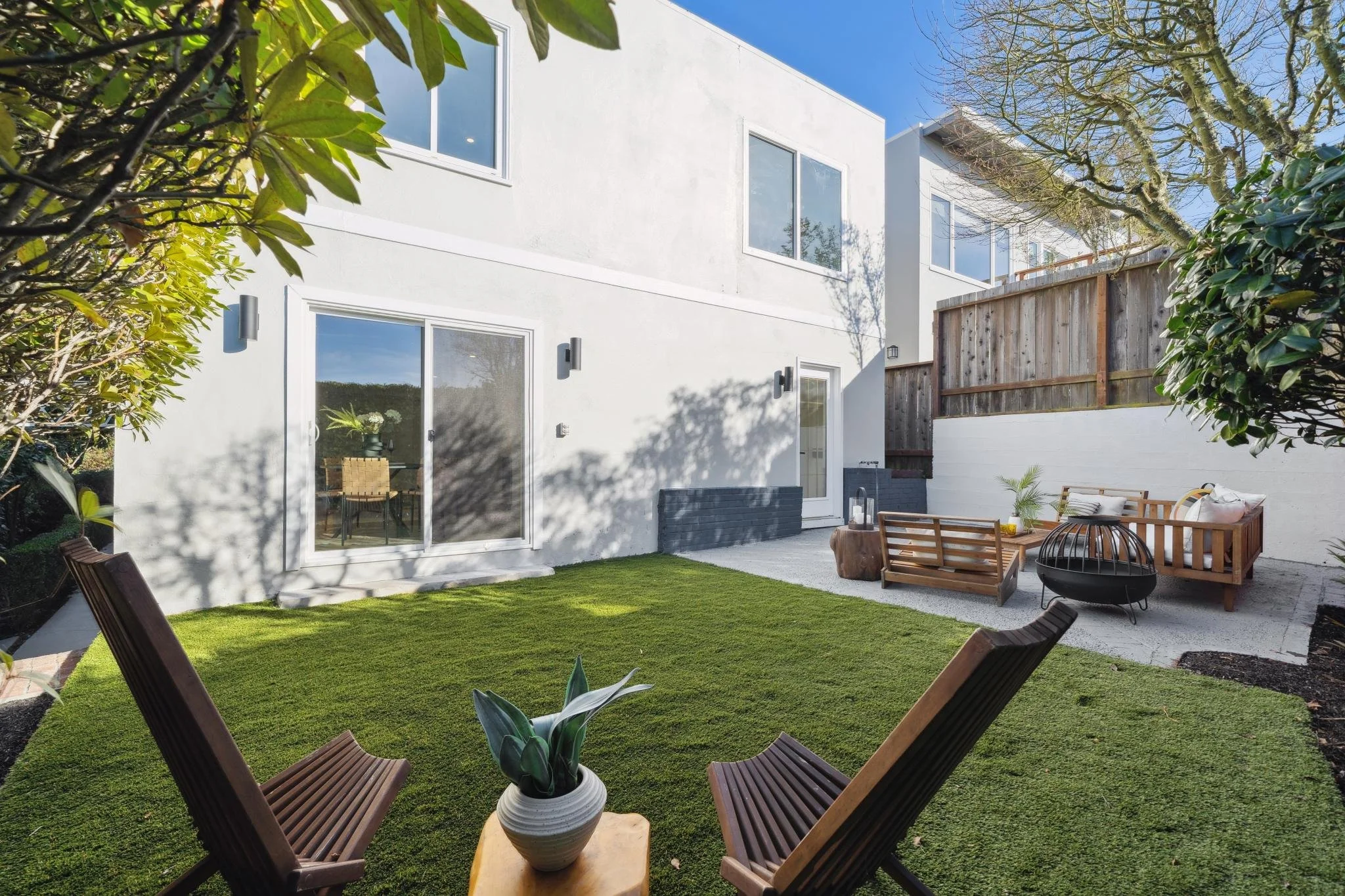 Private San Francisco backyard featuring a flat synthetic lawn, a gravel patio with a fire pit, and wooden lounge furniture.