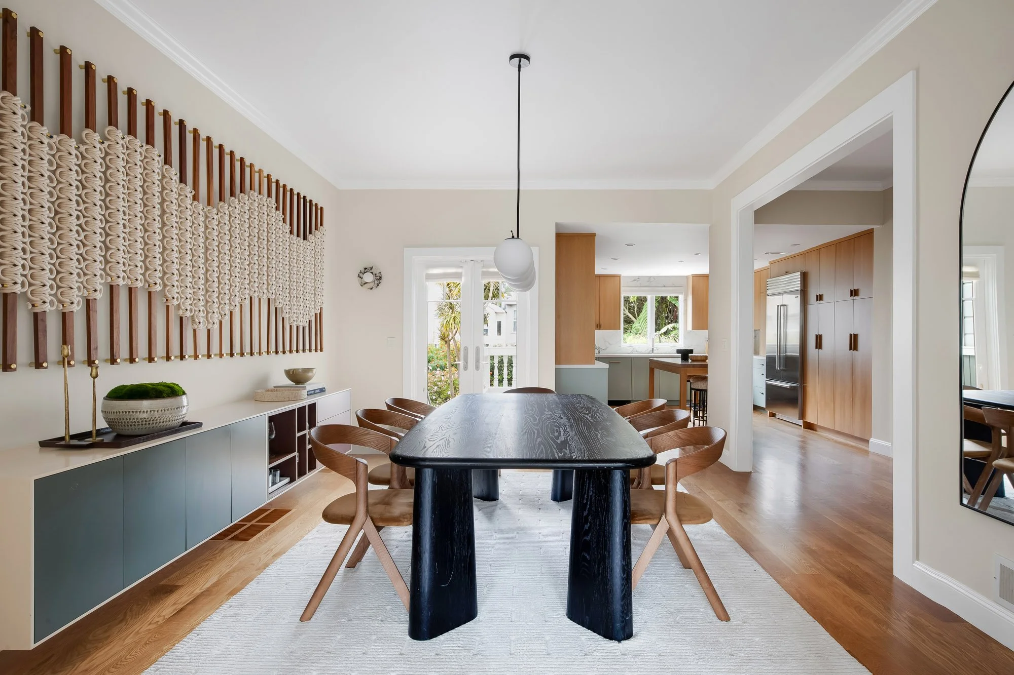 Dining room at 771 Elizabeth Street opening to the kitchen, showing the Windy Chien art wall, custom credenza, globe pendant, and French doors to the rear garden with the Sub-Zero refrigerator visible beyond.