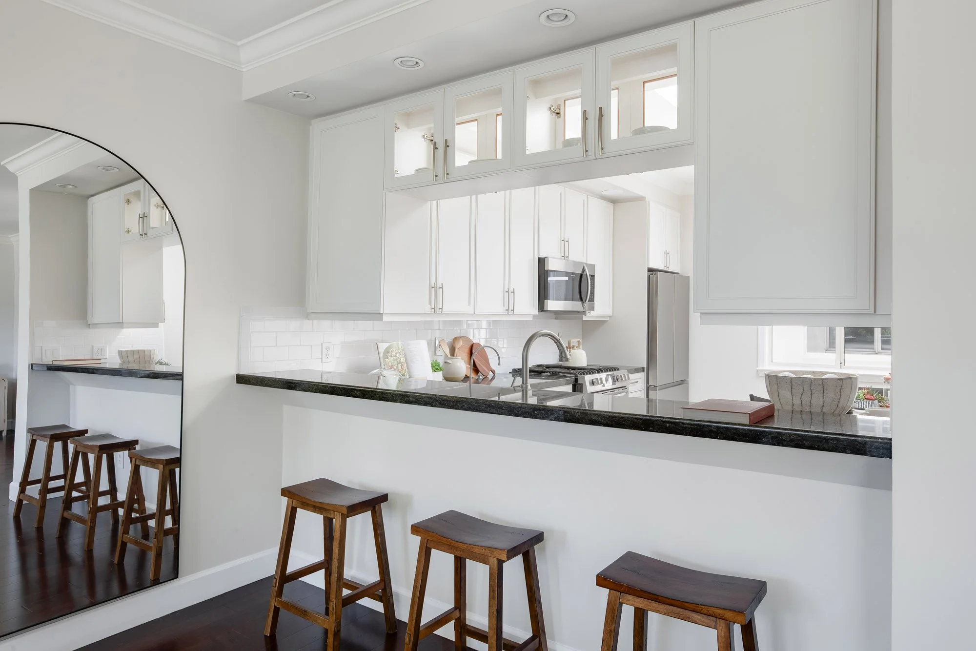 Kitchen bar and pass-through at 2172 Fell Street San Francisco with dark granite countertop, white shaker cabinets with glass fronts, saddle bar stools, subway tile backsplash, and stainless steel appliances