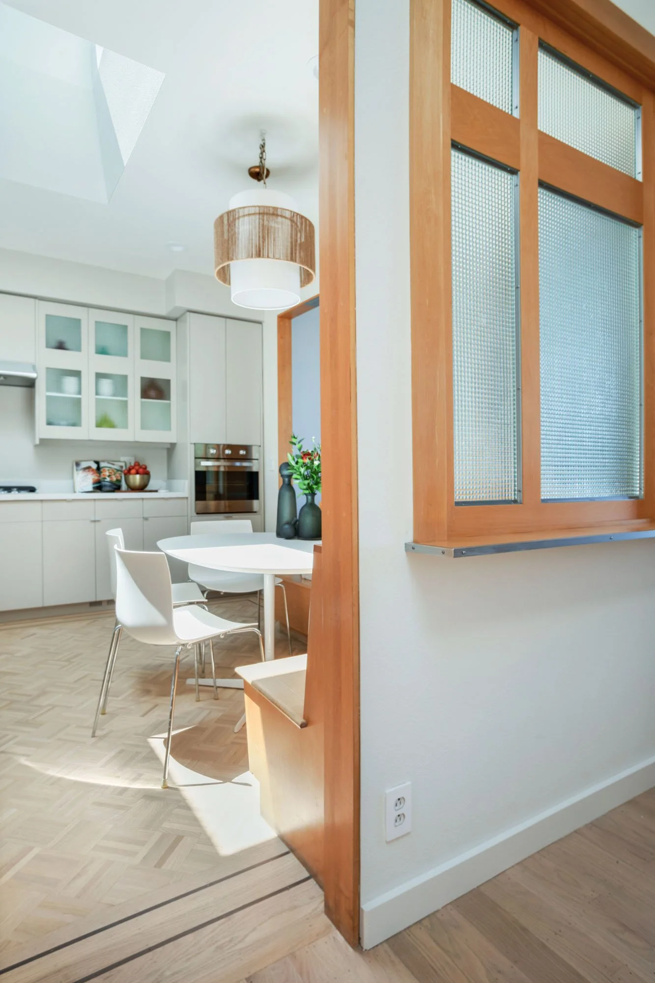 Architectural view of a San Francisco home's interior showing the seamless flow from a wood-accented dining nook into a modern kitchen with a large skylight.