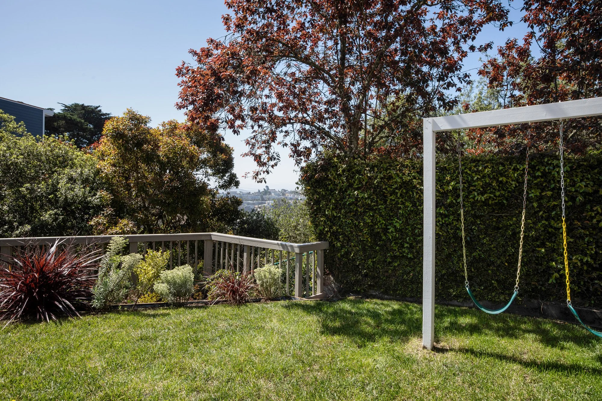 Spacious green backyard with a white swing set and a view of the surrounding hills and neighborhood.