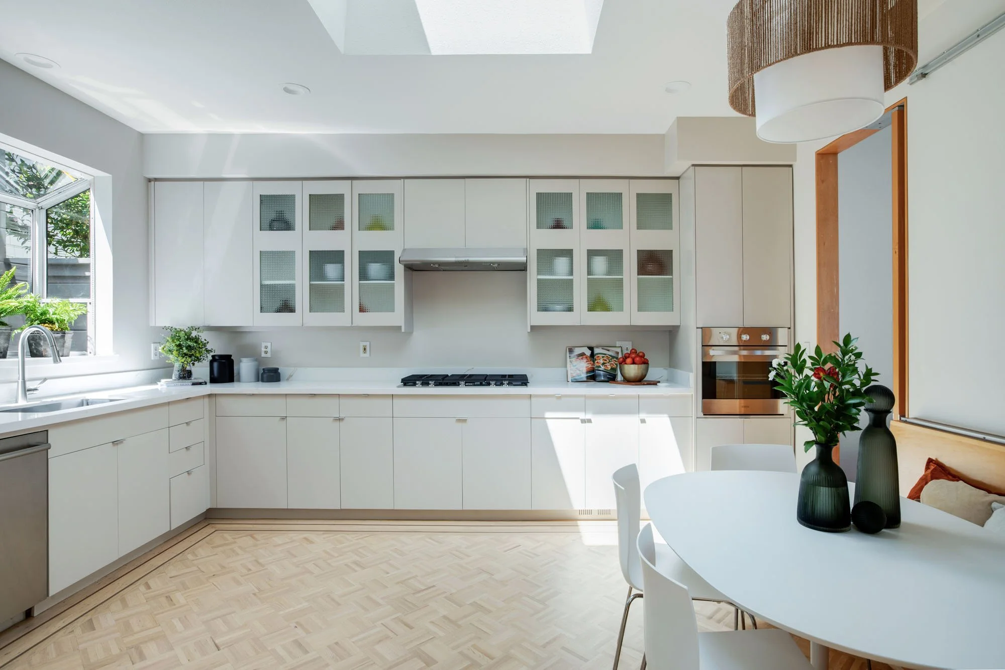 Modern minimalist kitchen featuring off-white cabinetry, a skylight for natural light, and a custom light-wood parquet floor with a dark wood inlay border.