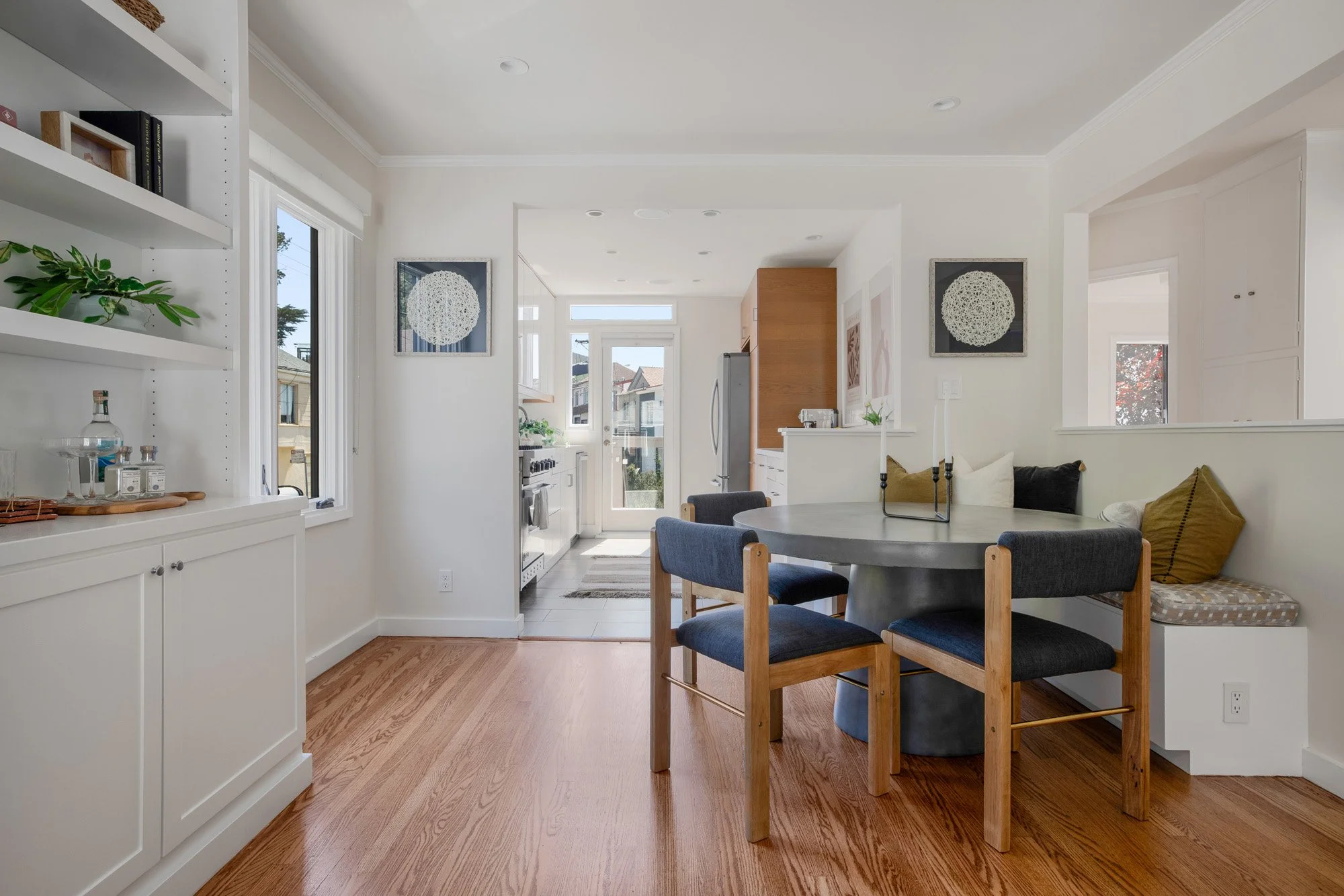 Open-concept dining room with a round concrete table, blue upholstered chairs, and a cozy built-in window seat.