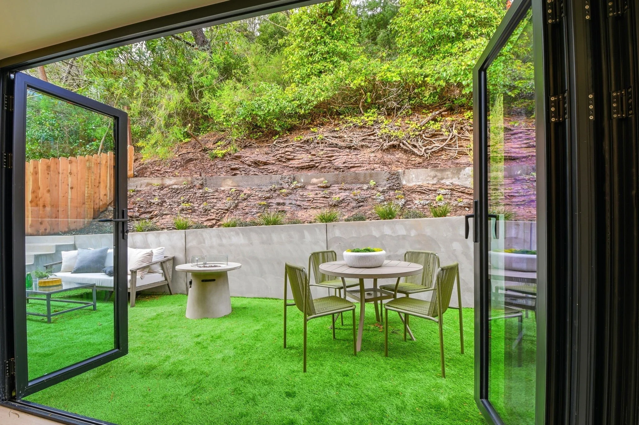 Private outdoor oasis in Midtown Terrace featuring artificial turf, a modern dining set, and black bifold glass doors for seamless indoor-outdoor living.
