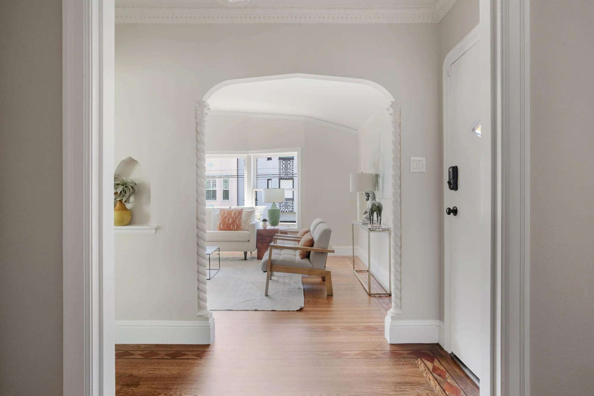 Interior view of a luxury San Francisco home featuring an arched entryway with decorative barley-twist columns and original inlaid hardwood floors.