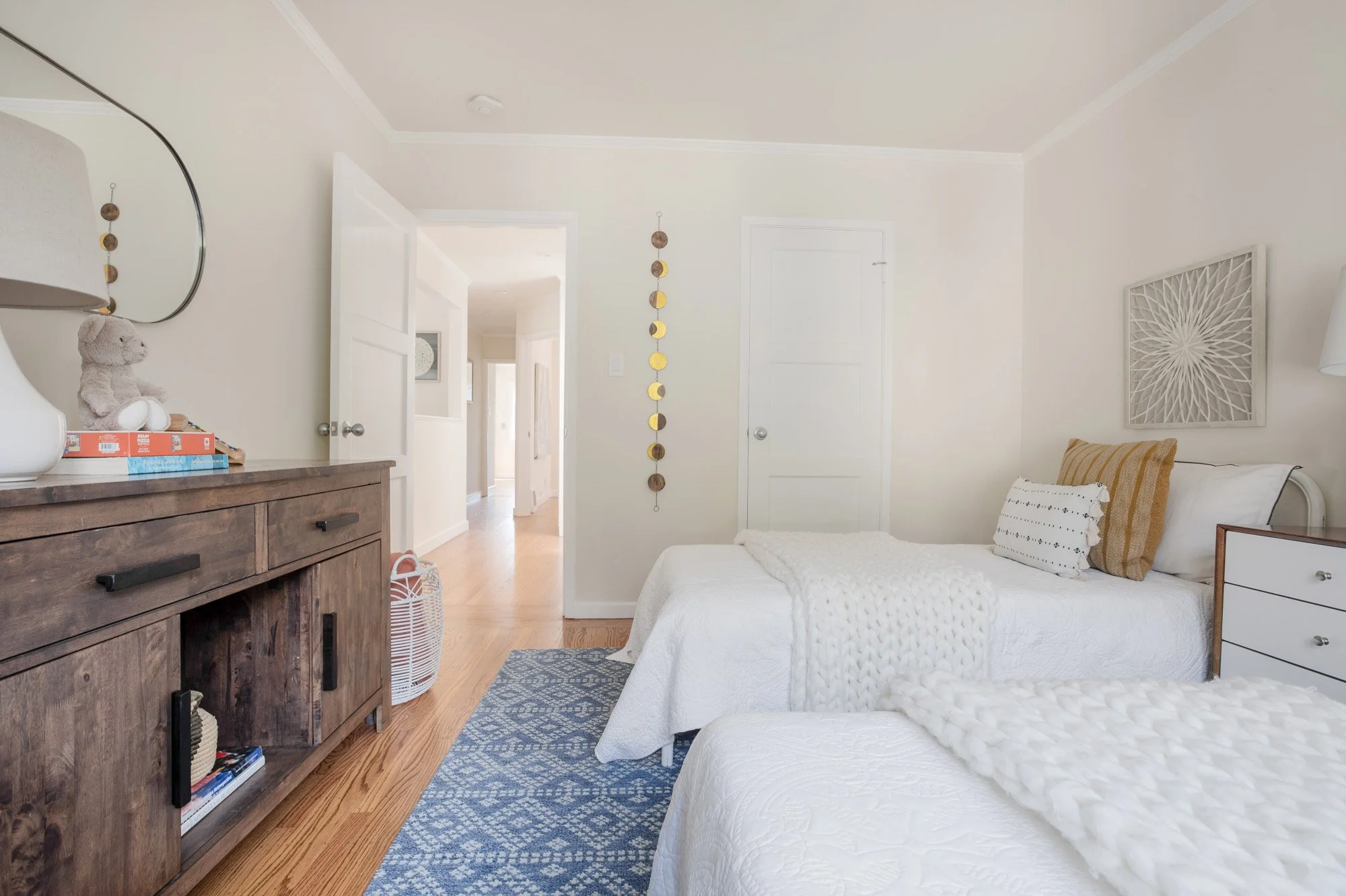 Bright guest bedroom or kids' room with hardwood floors, neutral walls, and a large window overlooking lush greenery.