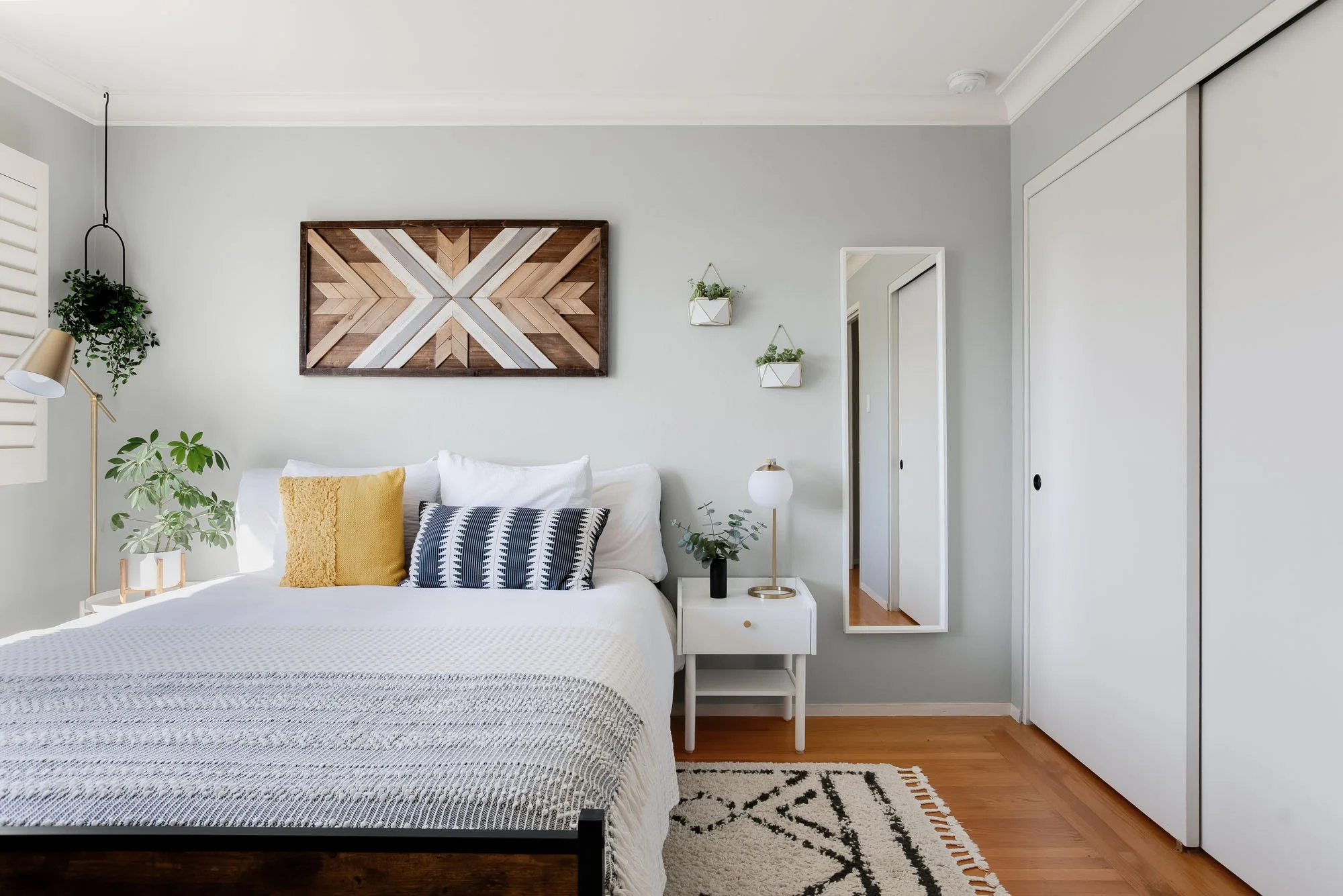 Symmetrical shot of a guest bed with a yellow accent pillow, white nightstand, and wall-mounted planters.