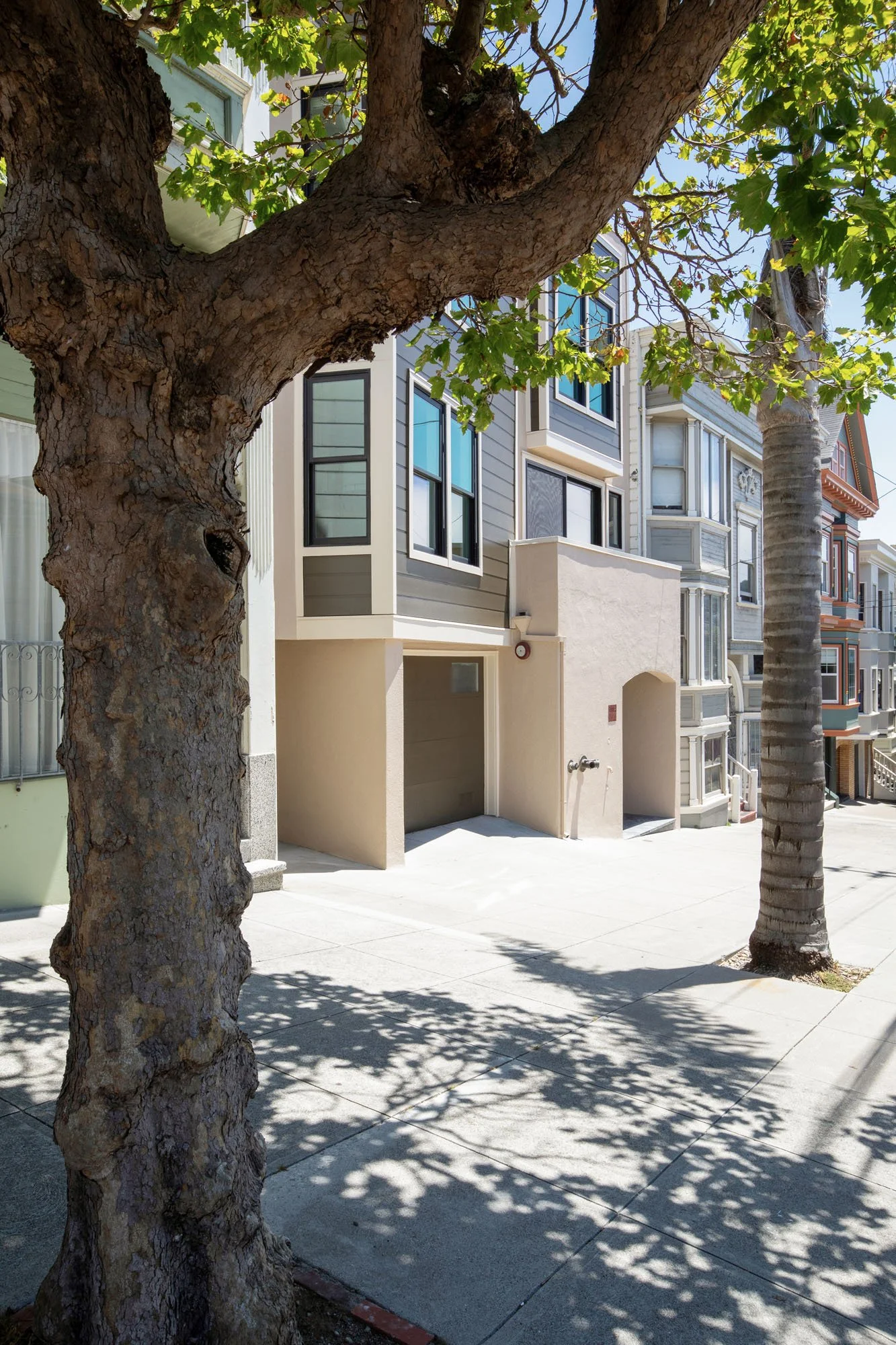 Street-level view of a modern contemporary home on a sloped city street featuring a private garage and a minimalist arched entryway.