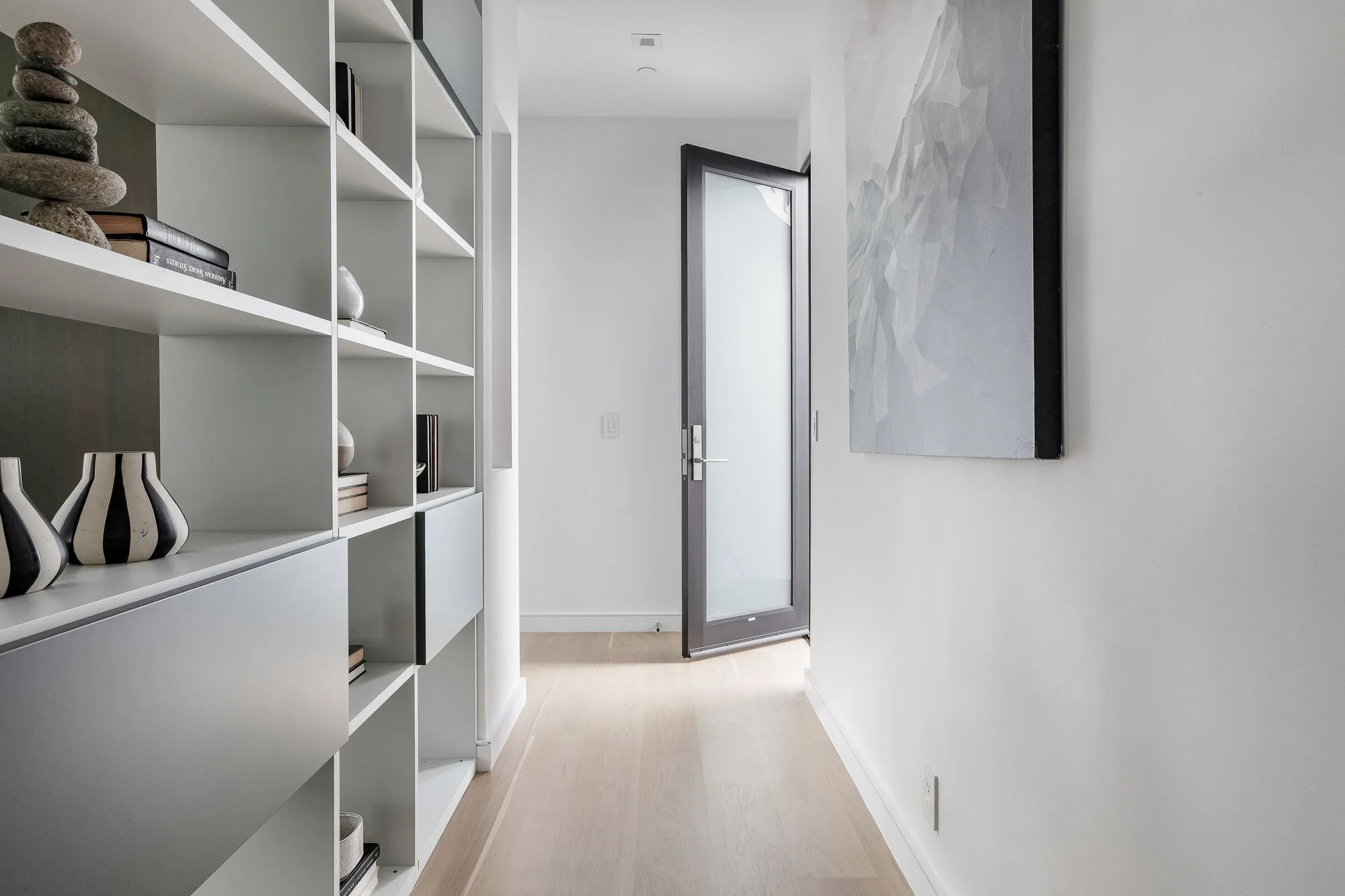 Minimalist modern hallway at 1647 Sanchez featuring custom white built-in bookshelves, light oak floors, and a glass-paneled entry door with direct access from 3rd floor to garden terrace.