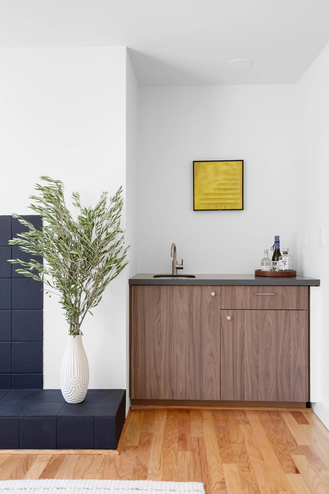 Built-in walnut wet bar with sink and quartz counter beside the black-tiled fireplace in the living room at 932 Broderick Street #2.