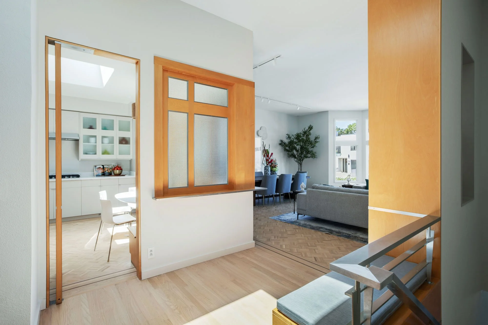 View from a light-filled hallway looking into a formal dining room and living area, showcasing the rich wood accents and custom parquet flooring details.