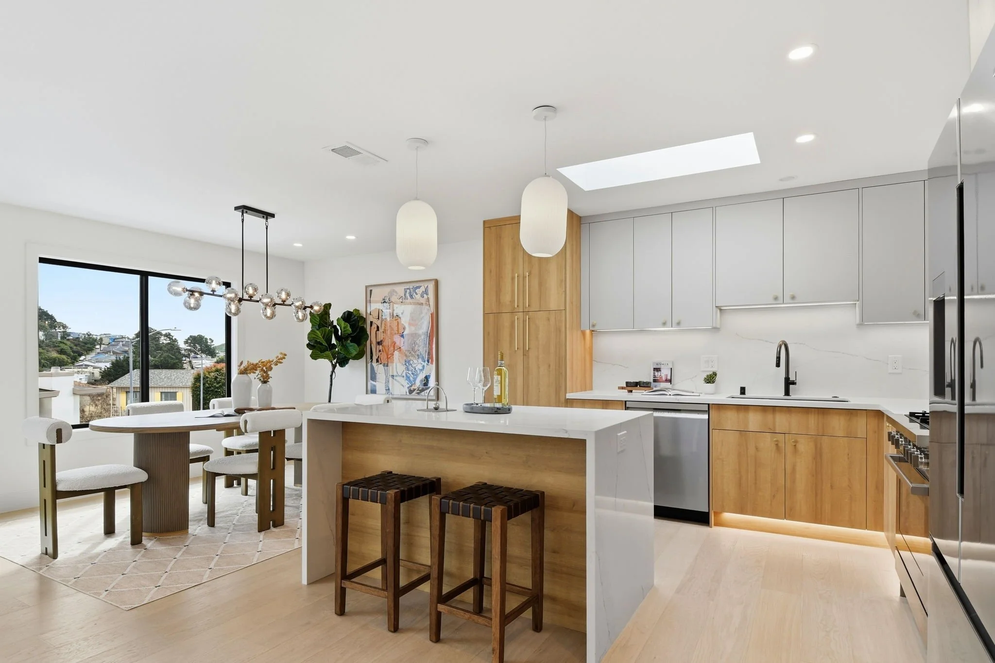 Modern designer kitchen in San Francisco featuring a marble waterfall island, light wood cabinetry, skylight, and professional-grade stainless steel appliances.