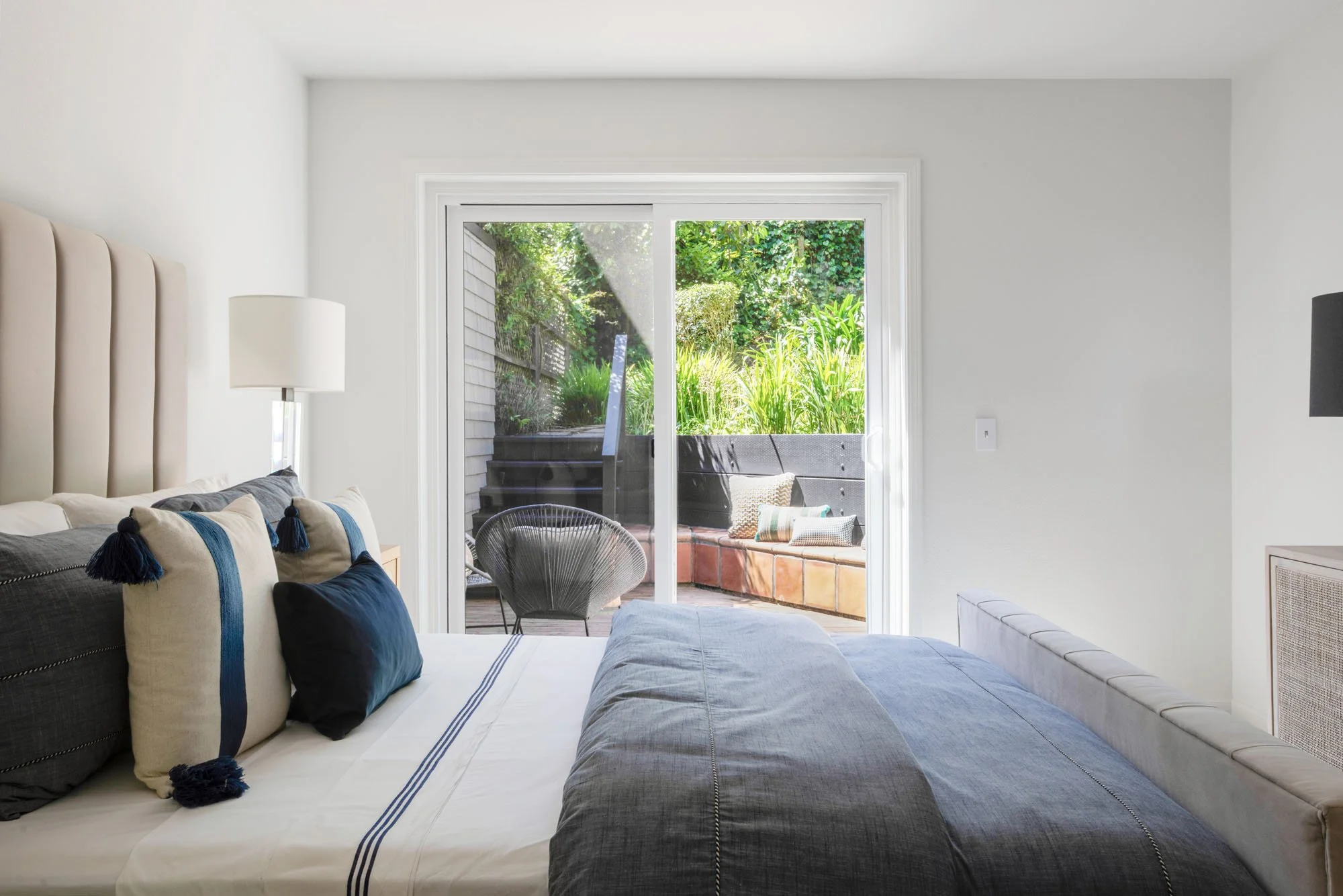 View from a primary bedroom looking through sliding glass doors onto a tiered private patio with a built-in bench and lush San Francisco garden landscaping.