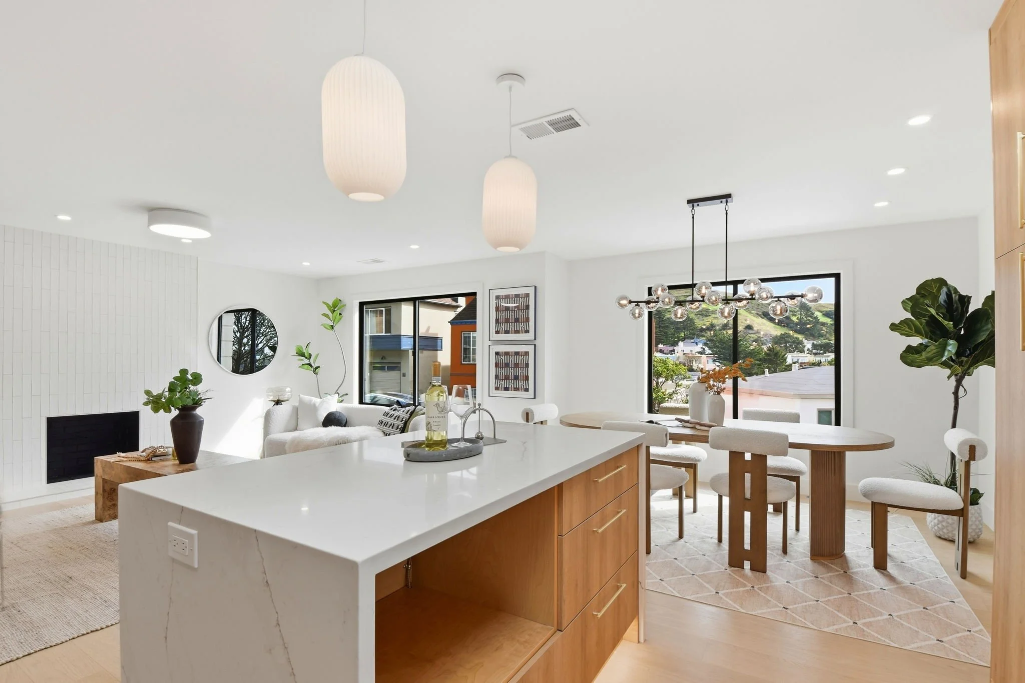 View from the kitchen island toward a formal dining area with a modern globe chandelier and panoramic hillside views in Midtown Terrace.