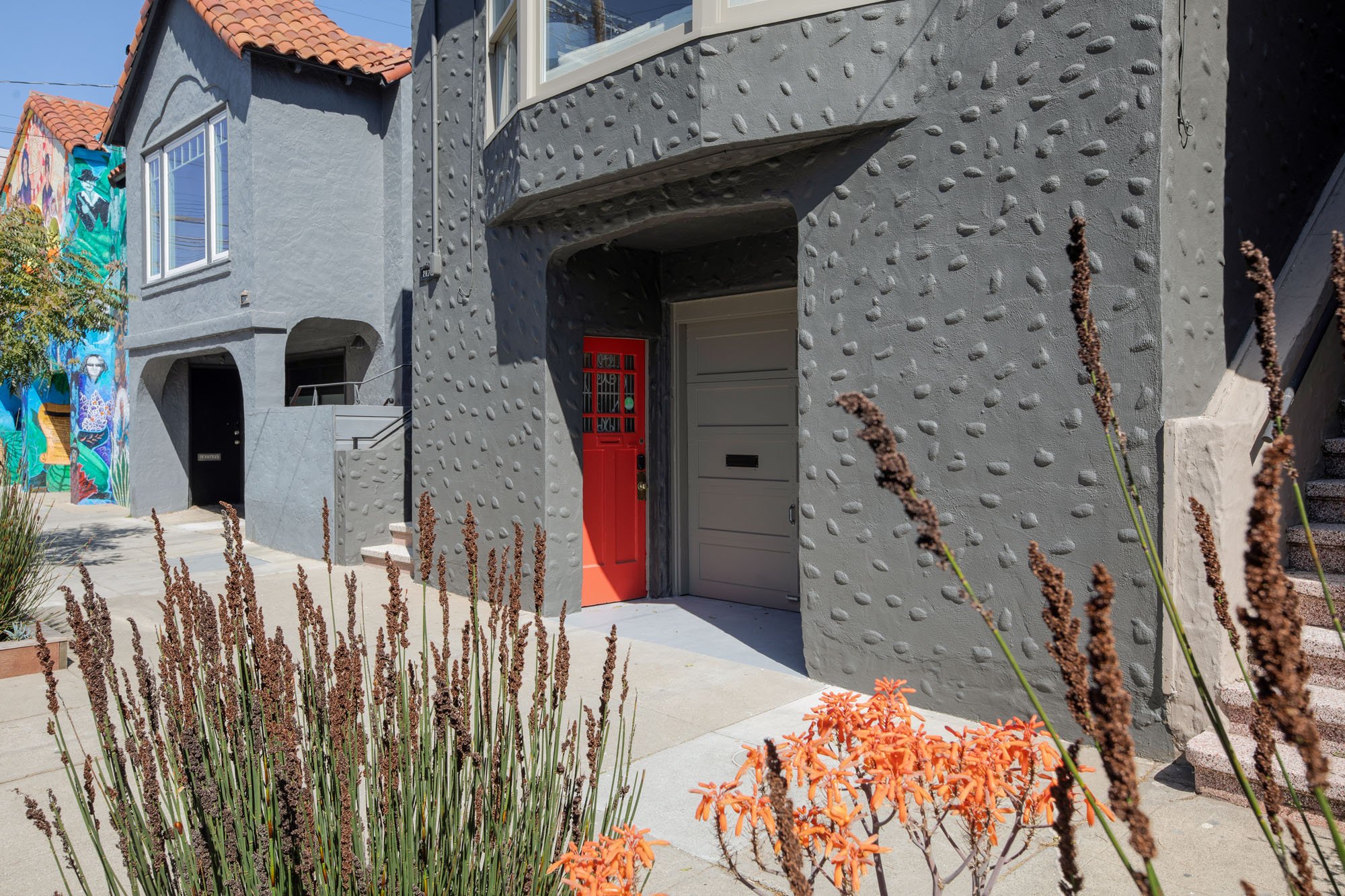 Close-up of the modern charcoal exterior and vibrant red front door of a renovated Mission District home with drought-tolerant landscaping.