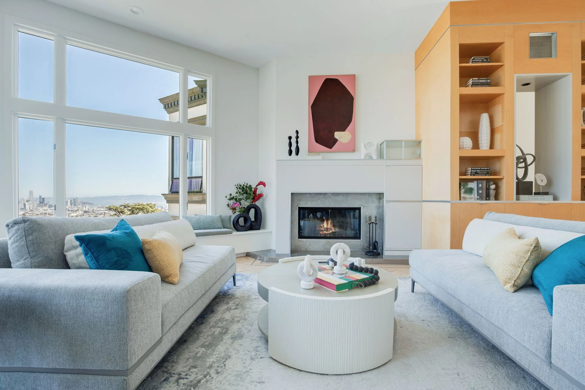 Modern San Francisco living room interior featuring grey upholstered sofas, a minimalist white fireplace, and large bay windows overlooking the city.