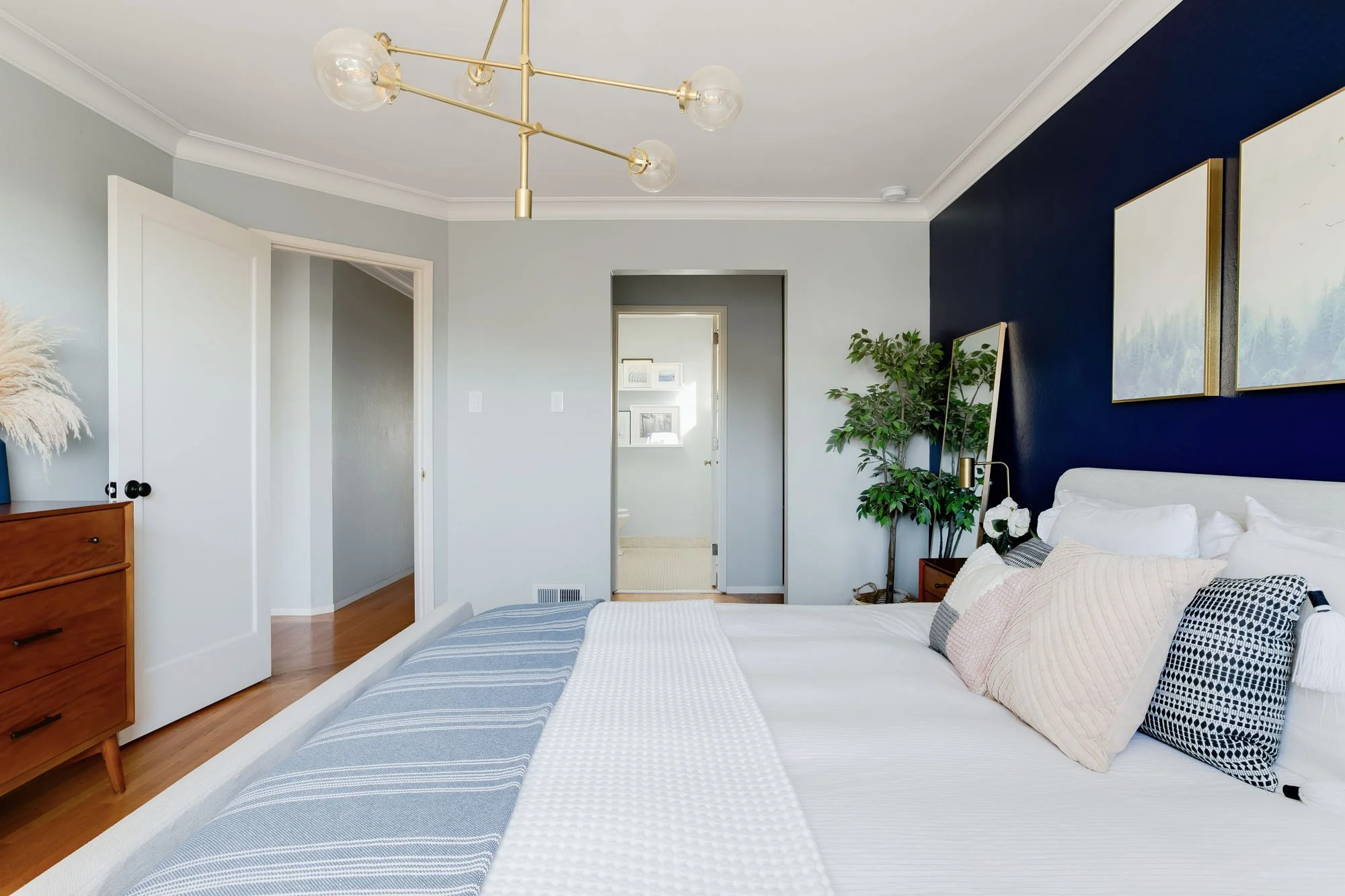 View from the bed looking toward the hallway and ensuite bathroom, showing light gray walls, hardwood floors, and a vintage-style wood dresser