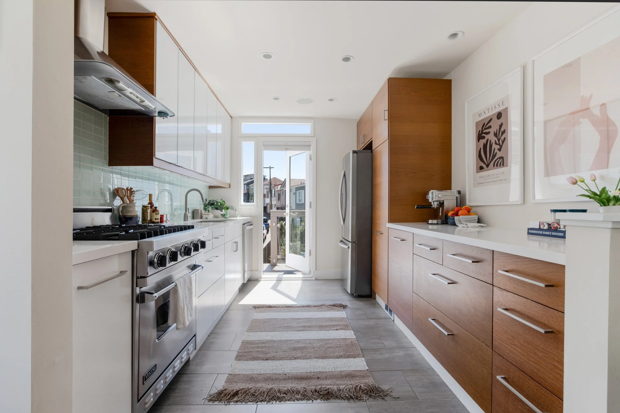 Modern galley kitchen featuring a professional Viking gas range, stainless steel appliances, and sleek wood cabinetry with an open back door.