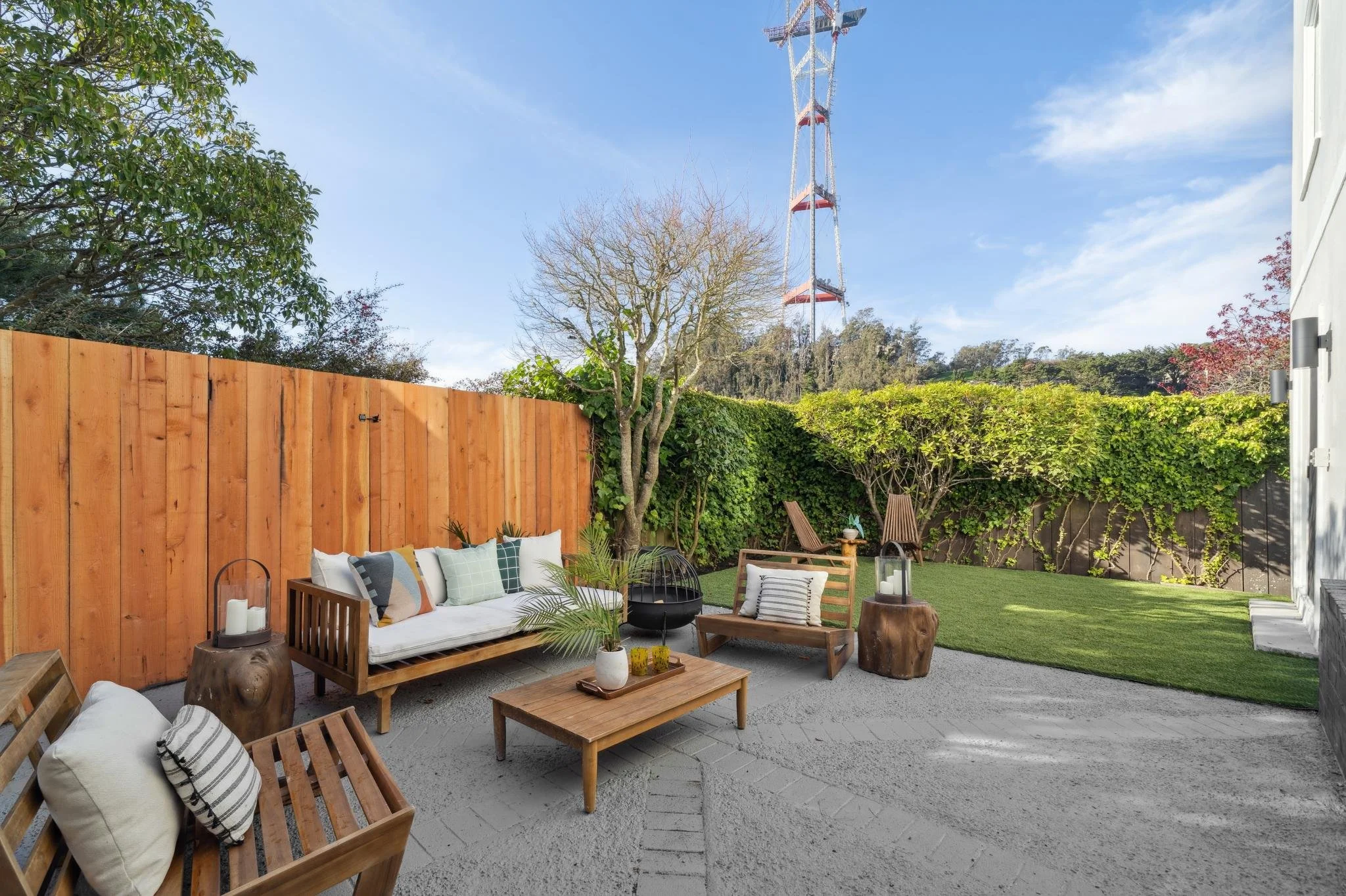 Private paved backyard at 147 Gladeview Way with a wooden outdoor sofa, fire pit, and synthetic lawn, featuring a clear view of Sutro Tower.