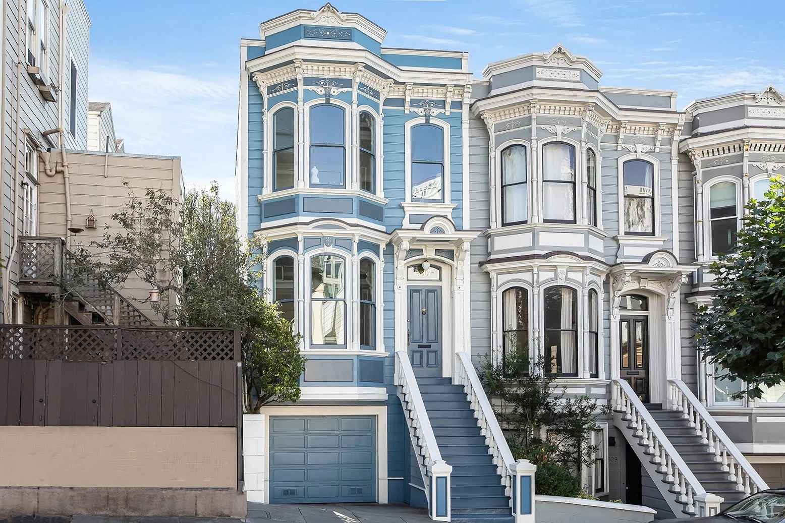 Front exterior of a classic blue-painted luxury Victorian home in San Francisco with ornate architectural detailing and a formal grand staircase.