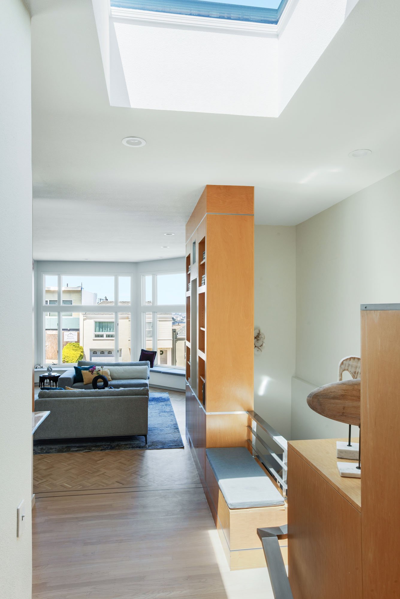 Perspective view of a modern San Francisco home layout, showing a custom wood library wall, built-in window seating, and a sun-drenched living room with city views.