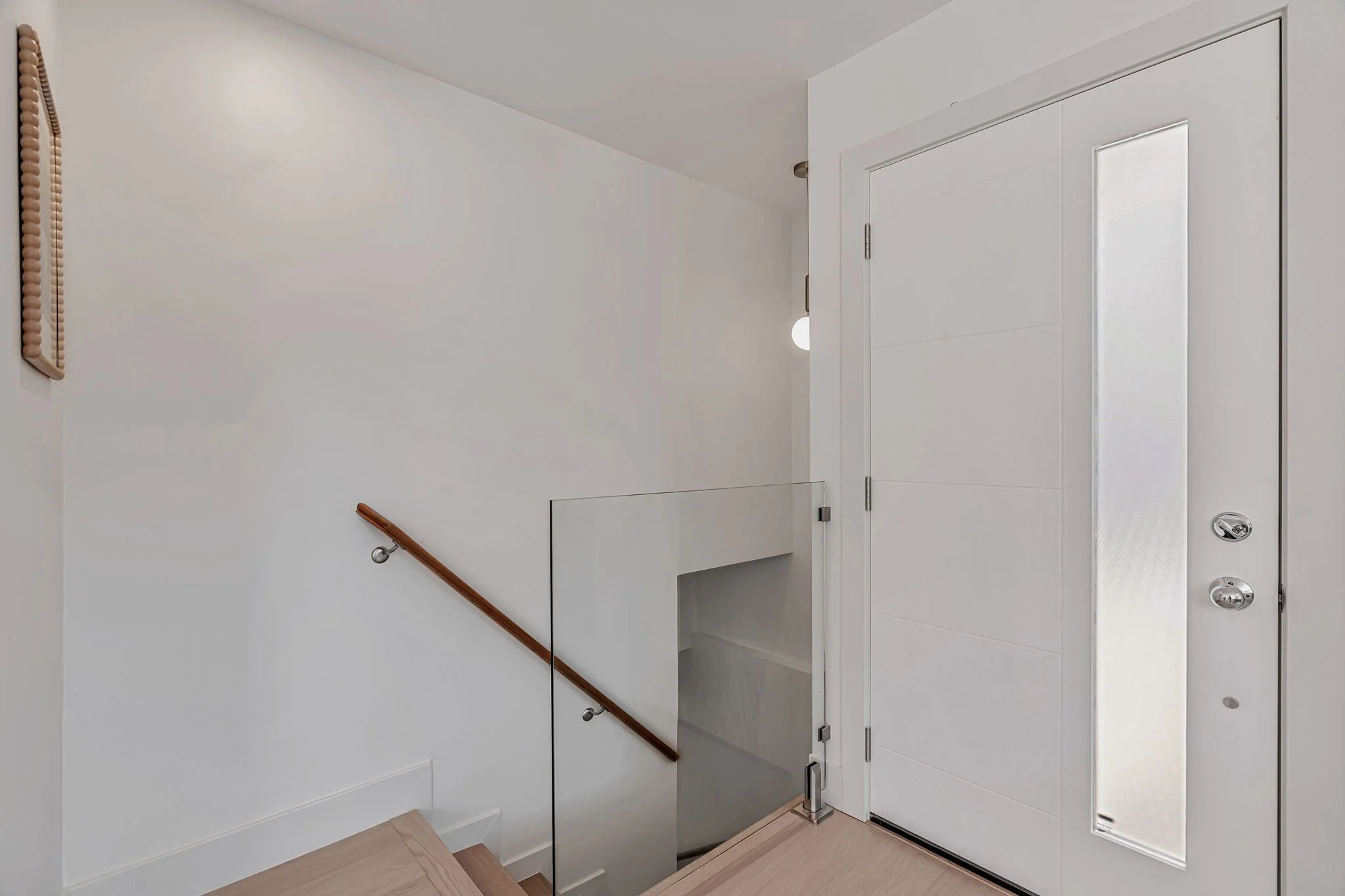 Modern luxury home entrance featuring a sleek white front door with a frosted glass sidelight and a contemporary glass-walled staircase.
