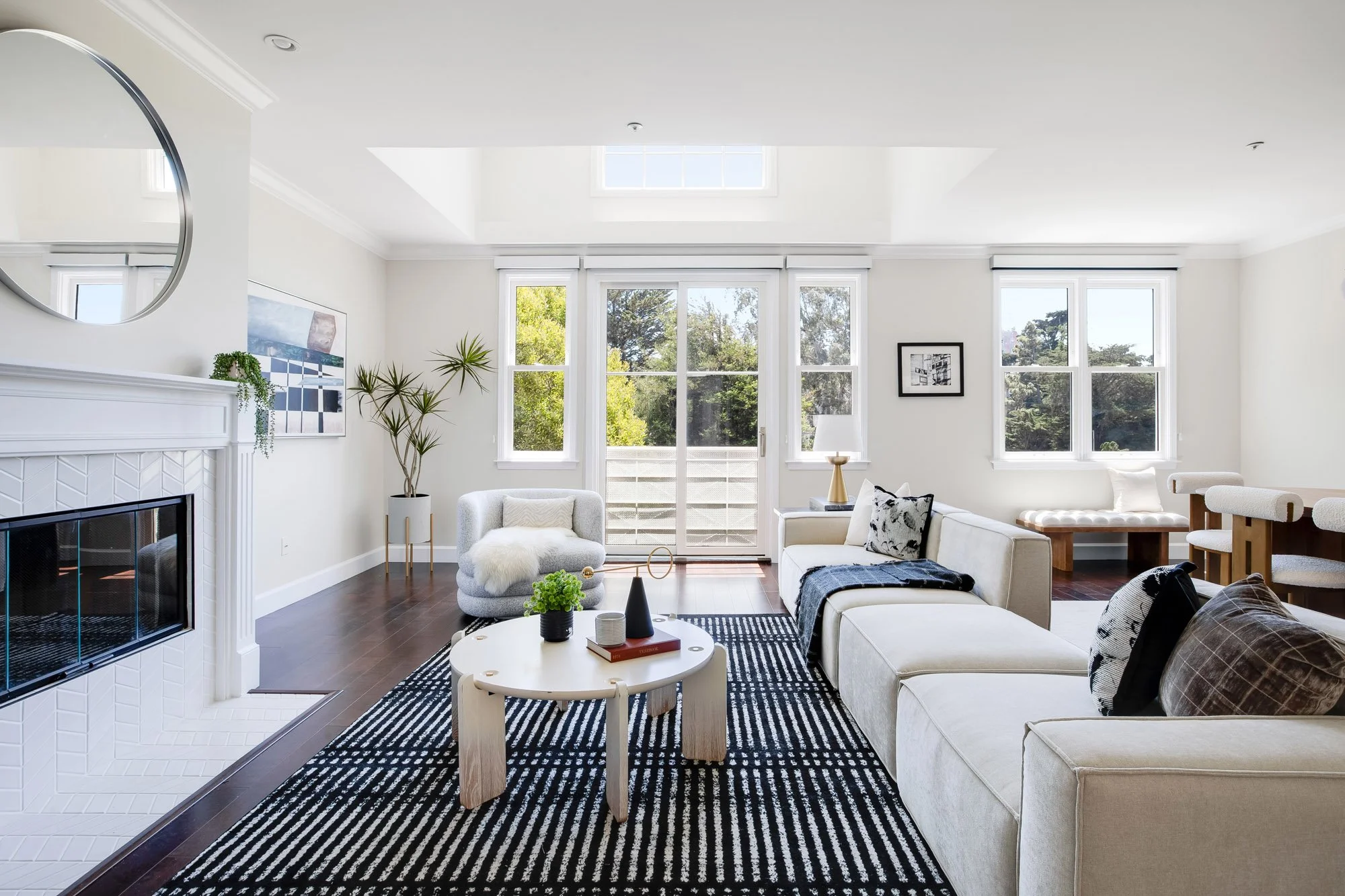 Sunlit living room at 2172 Fell Street San Francisco featuring a white herringbone fireplace, clear story skylight, cream boucle sofa, round sculptural coffee table, and French doors opening to a balcony