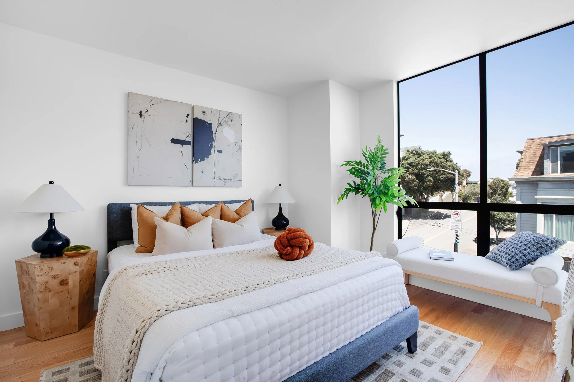 Bright second bedroom at 932 Broderick Street #2 with a blue upholstered bed, floor-to-ceiling corner windows, and a window-seat daybed overlooking the NoPa neighborhood.