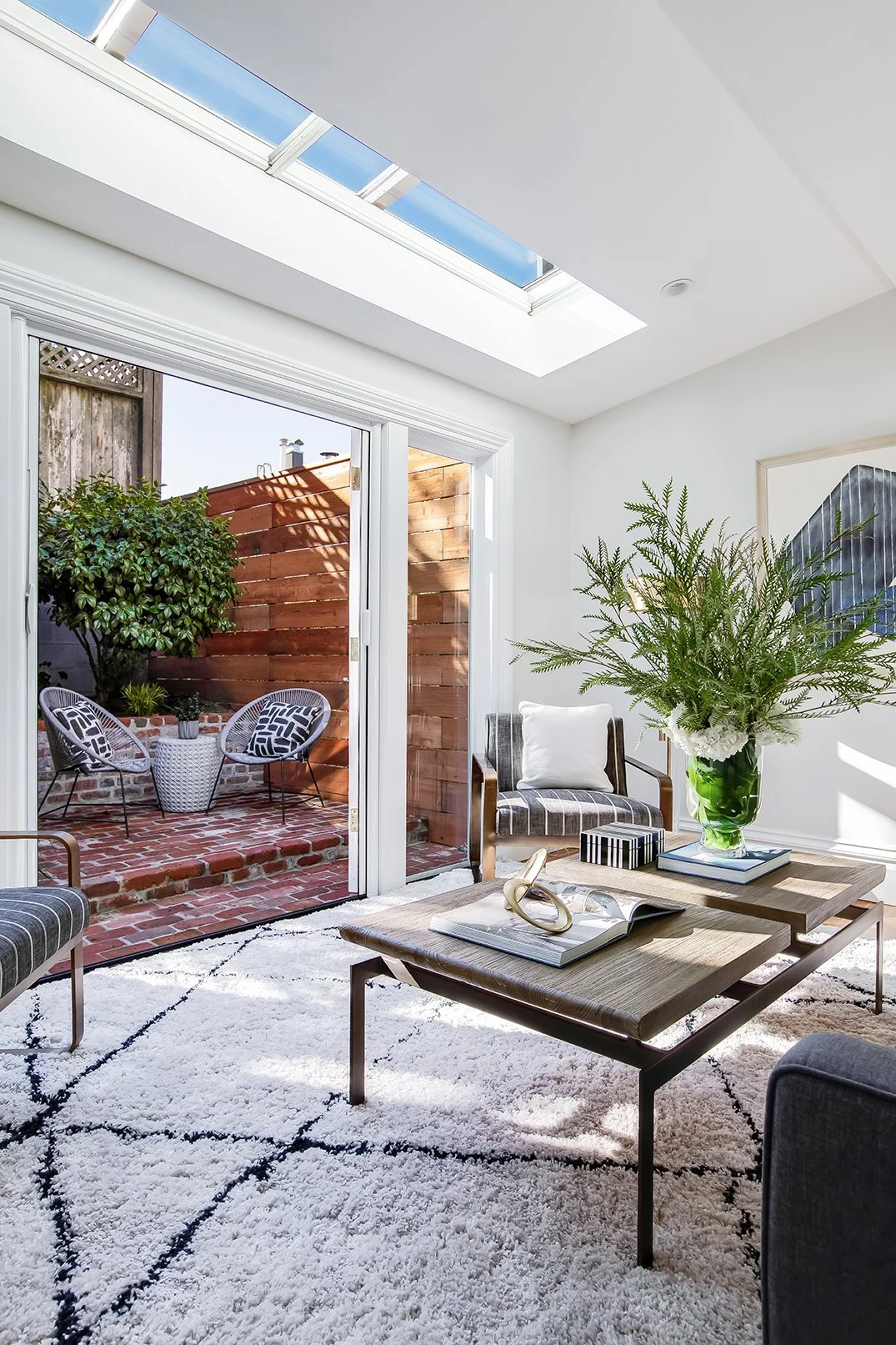 Light-filled contemporary living room with a large skylight and sliding glass doors leading to a private brick-paved patio.