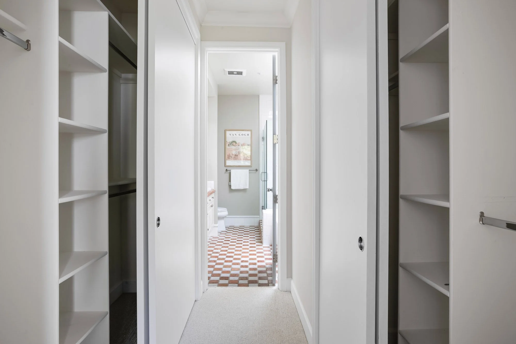 Walk-through closet with built-in white shelving and hanging rods leading to the en suite bathroom at 2172 Fell Street San Francisco, featuring terracotta checkerboard tile floors and glass shower enclosure