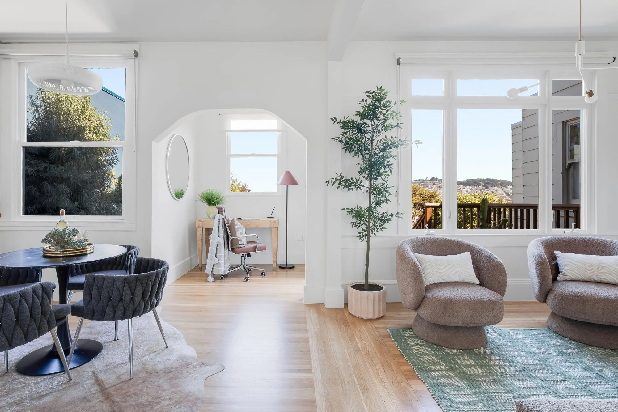 An open-concept main floor at 246 Detroit featuring a dining area with a black marble tulip table and an arched entryway leading to a sun-filled home office.
