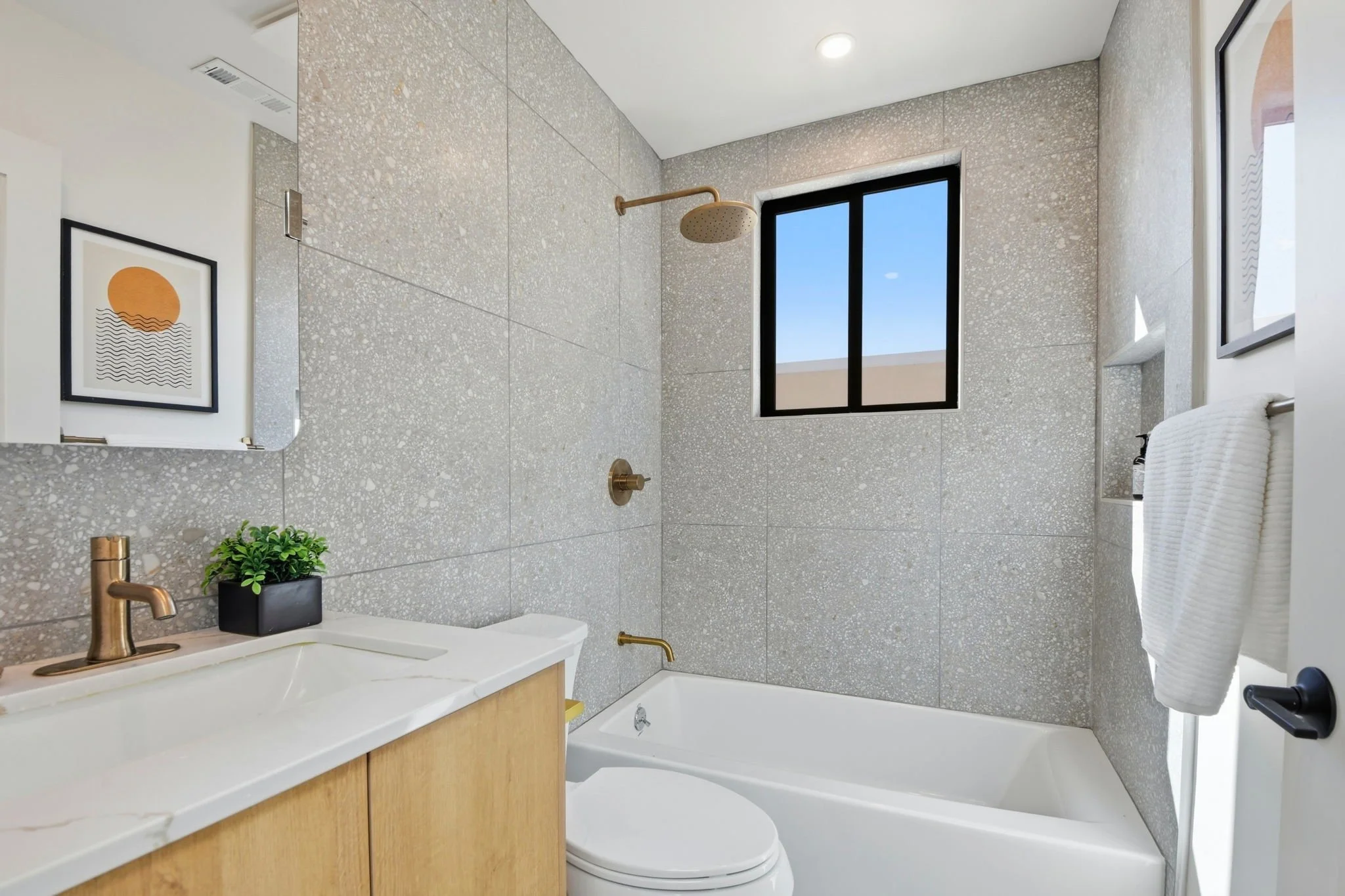 Spa-like bathroom in San Francisco featuring gray terrazzo-style wall tiles, a light wood vanity, and premium gold-toned fixtures.
