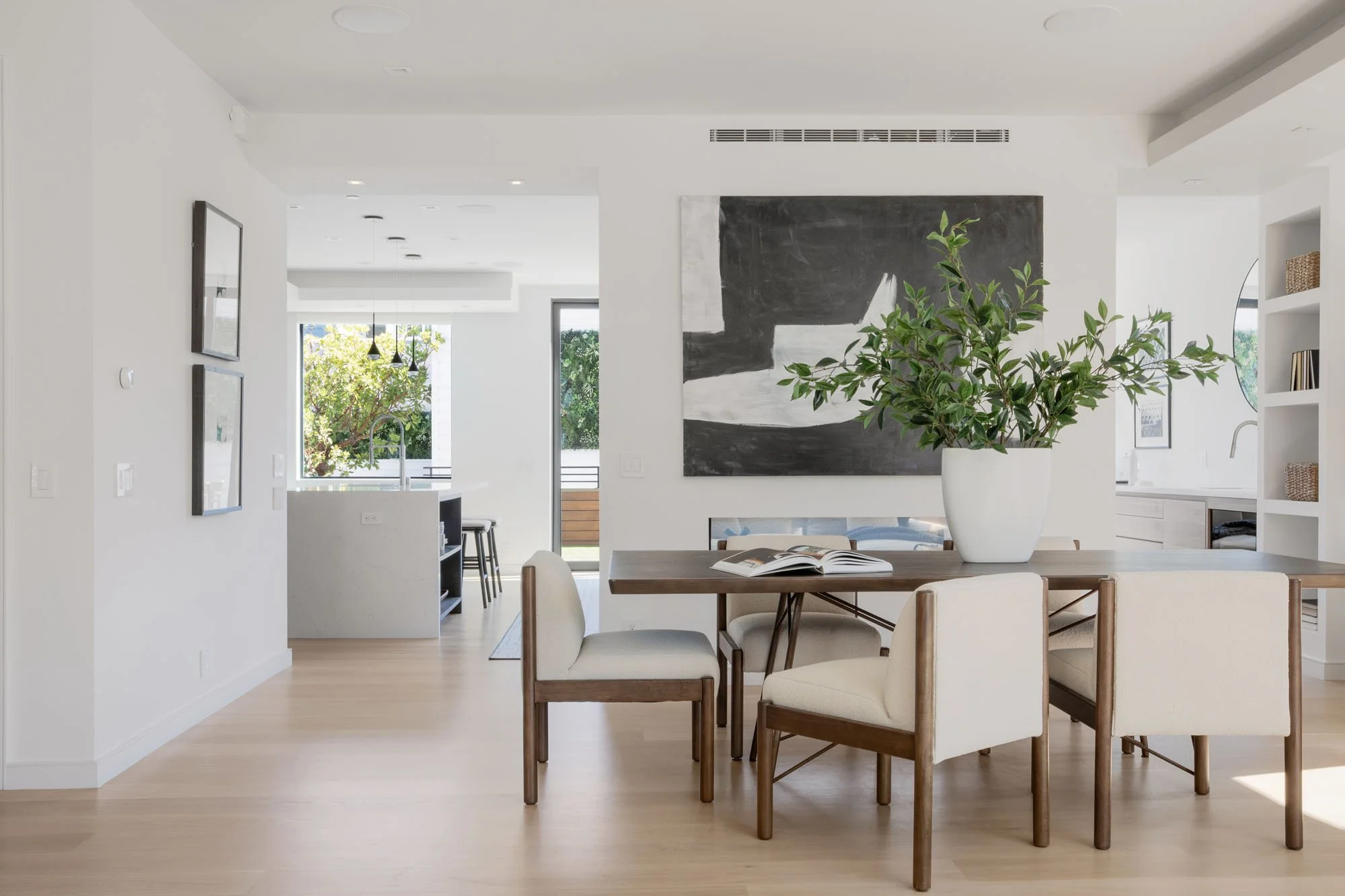 Modern dining room detail with a minimalist wood table, cream upholstered chairs, and a large green plant centerpiece in a bright, renovated Noe Valley home.