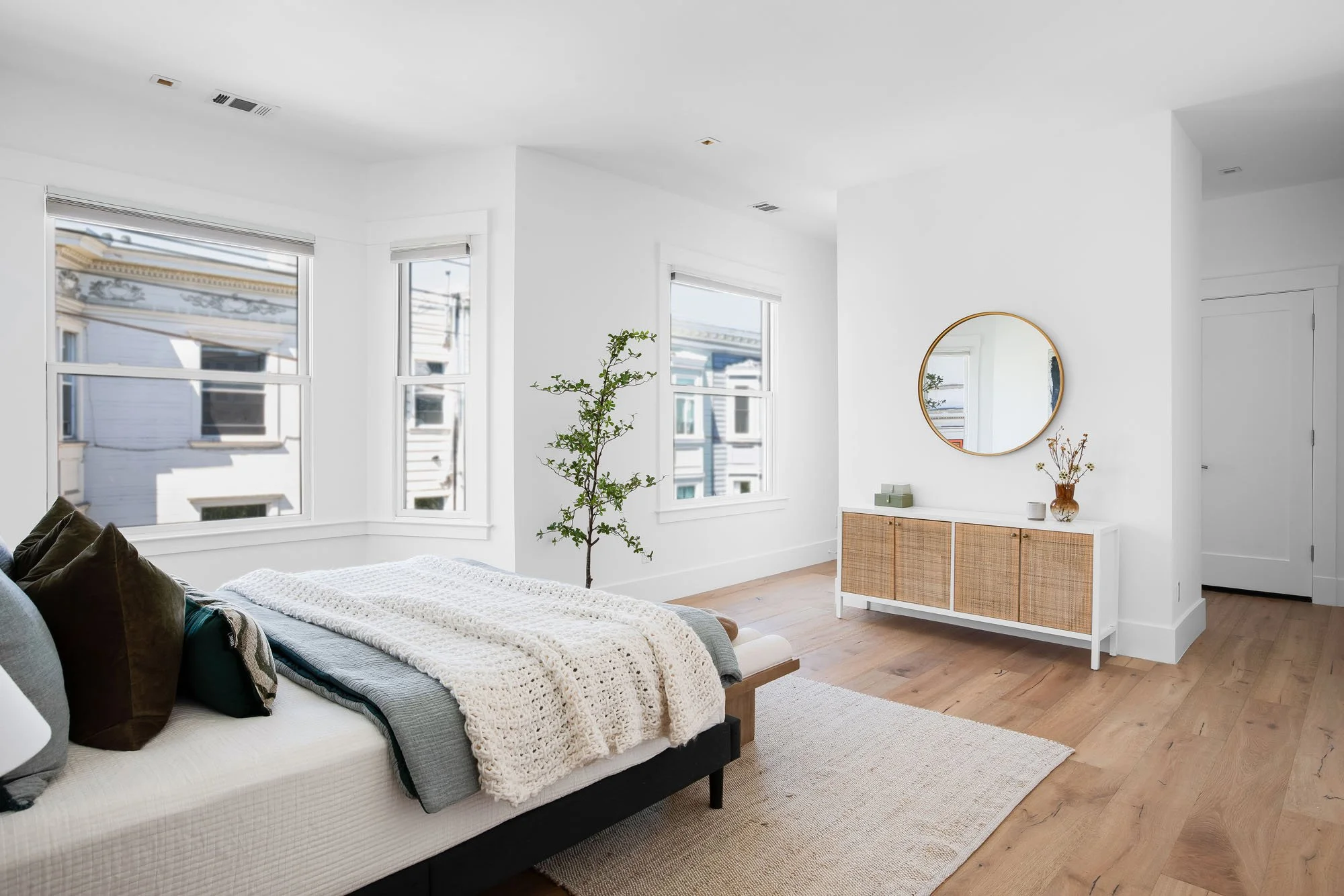 Primary suite in a San Francisco luxury home with classic bay windows, light oak floors, and a modern rattan sideboard.