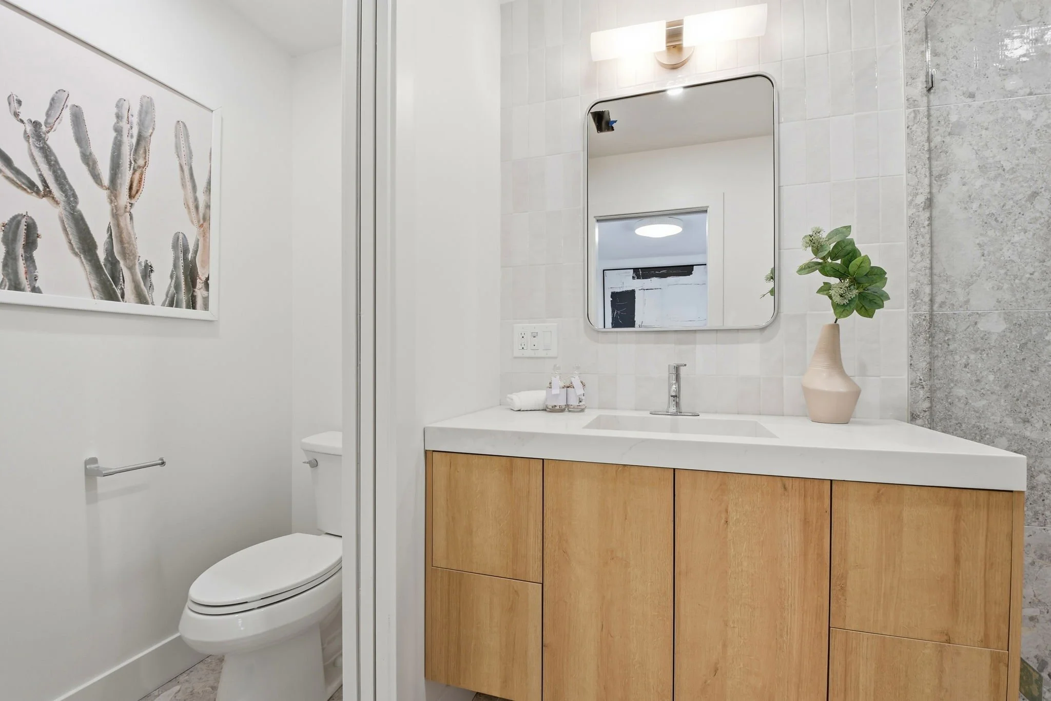 Close-up of a designer bathroom vanity with a white stone countertop, light wood cabinetry, and an elegant gold sconce in a renovated SF residence.
