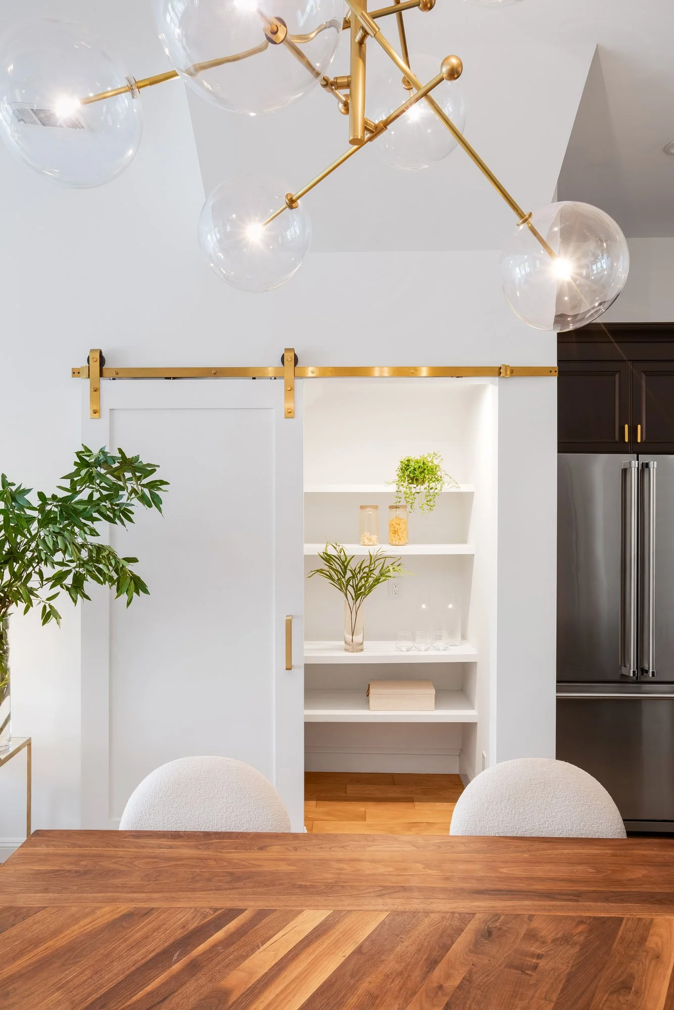 Gold sliding barn door revealing illuminated built-in pantry with white shelving at 4545 18th Street San Francisco TIC, flanked by brass Sputnik chandelier above walnut dining table and Viking refrigerator