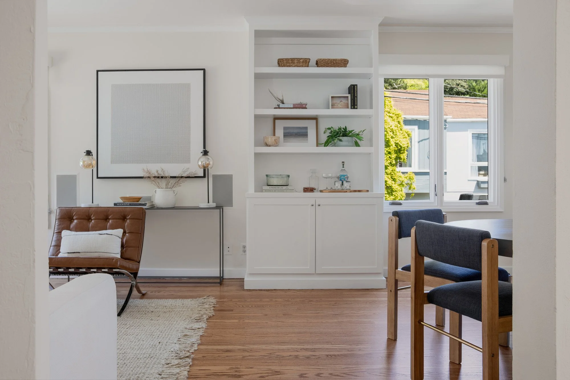 Bright dining area with built-in white shelving, a round concrete table, and a transition into the main living space.