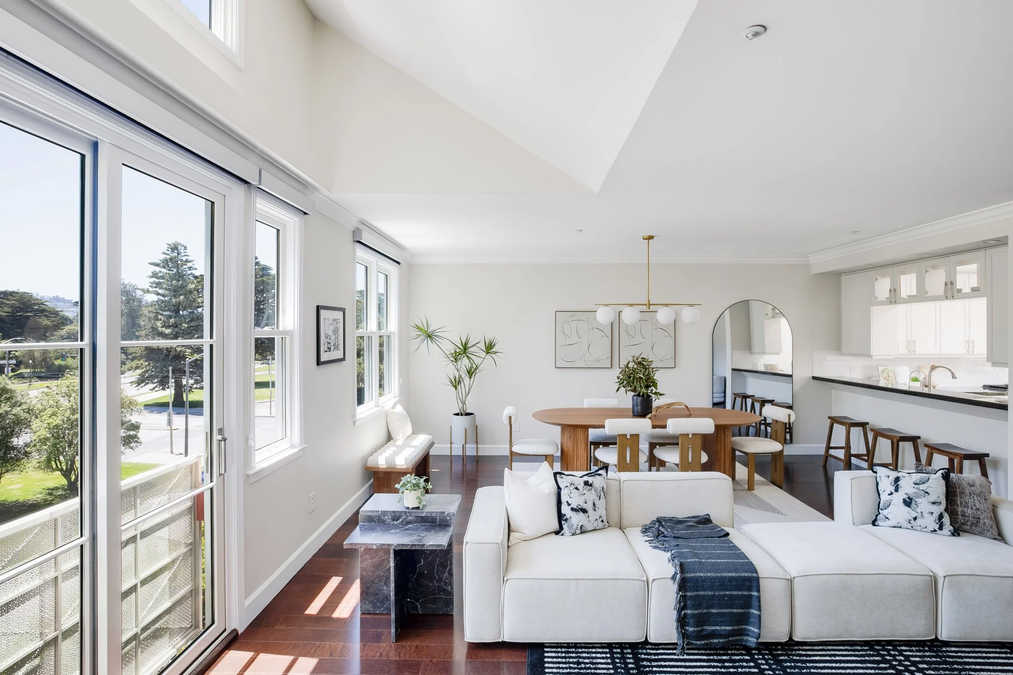 Expansive open-plan living, dining, and kitchen area at 2172 Fell Street San Francisco with floor-to-ceiling windows, dark marble coffee table, oval walnut dining table, and park views