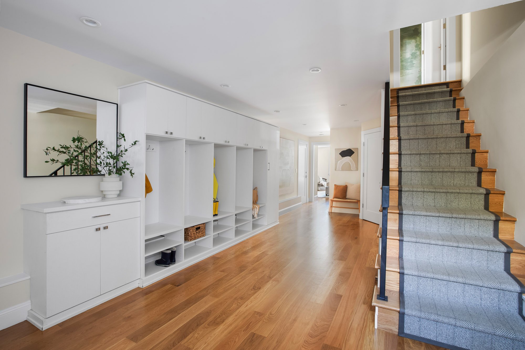 Lower-level hall at 771 Elizabeth Street in Noe Valley with a full wall of custom mudroom built-ins, open cubbies and bench seating, and a herringbone runner climbing the stair.