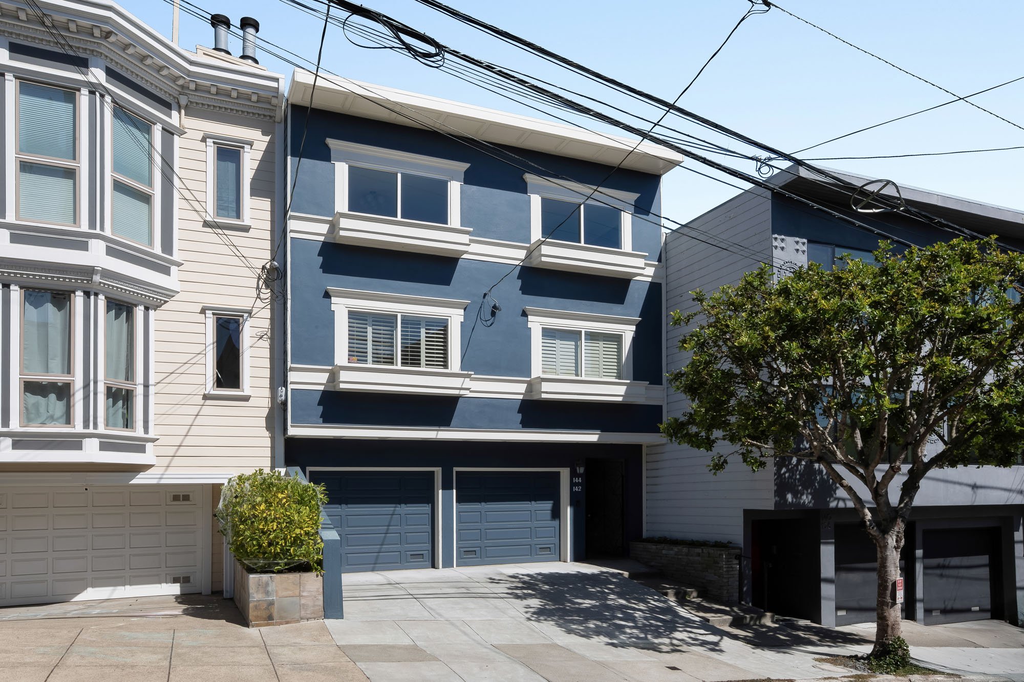 Front exterior of 144 Lower Terrace in San Francisco, featuring a bold navy blue facade with white architectural trim, bay windows, and a two-car garage.